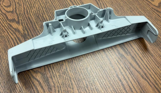 Gray plastic part with a large circular hole and textured grip areas, placed on a wooden surface.