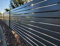 Modern horizontal slat fence with greenery and gravel on the ground