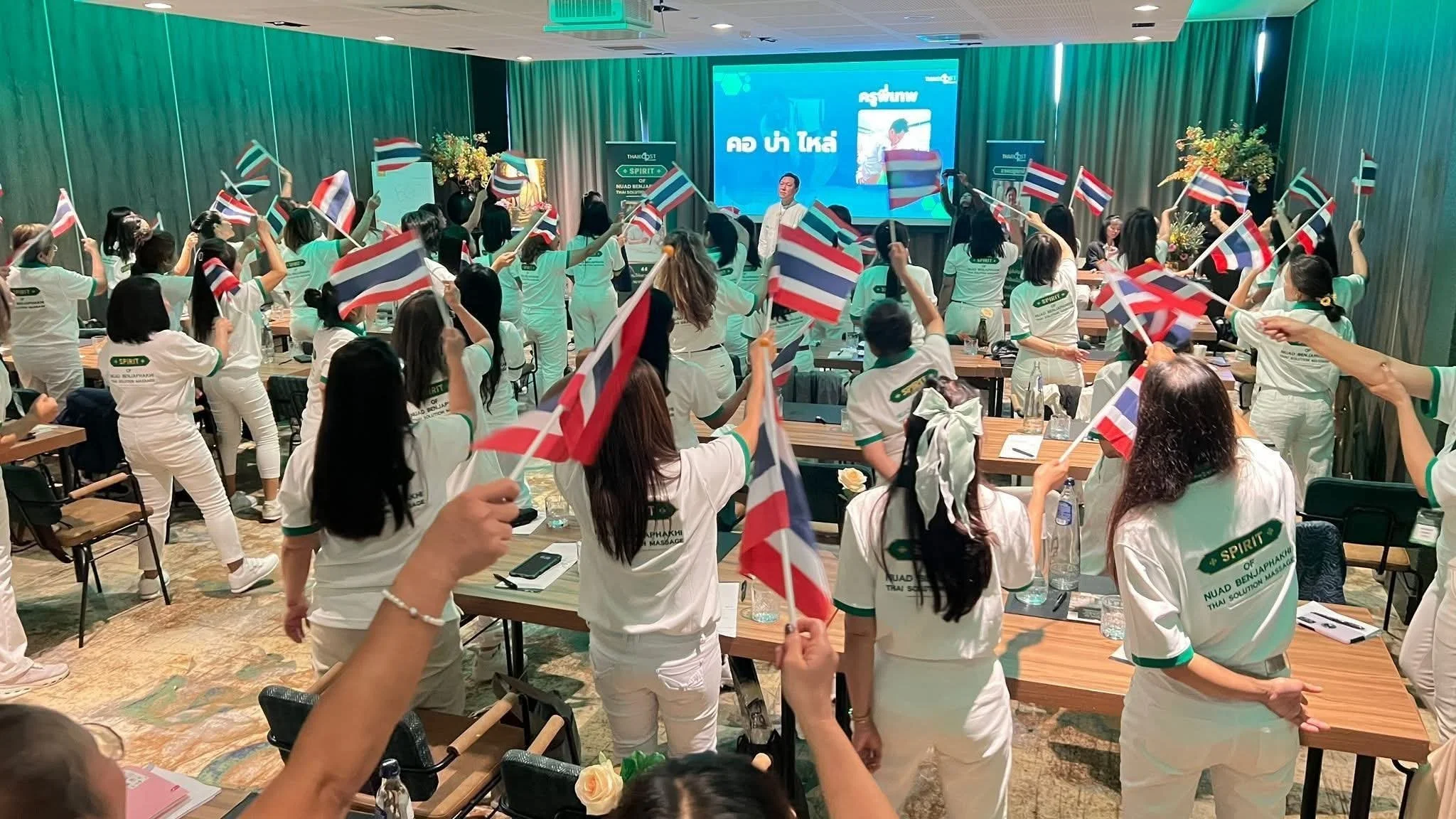 over 70 massage therapist waving Thai flags in a conference meeting for Thai Boost Academy 