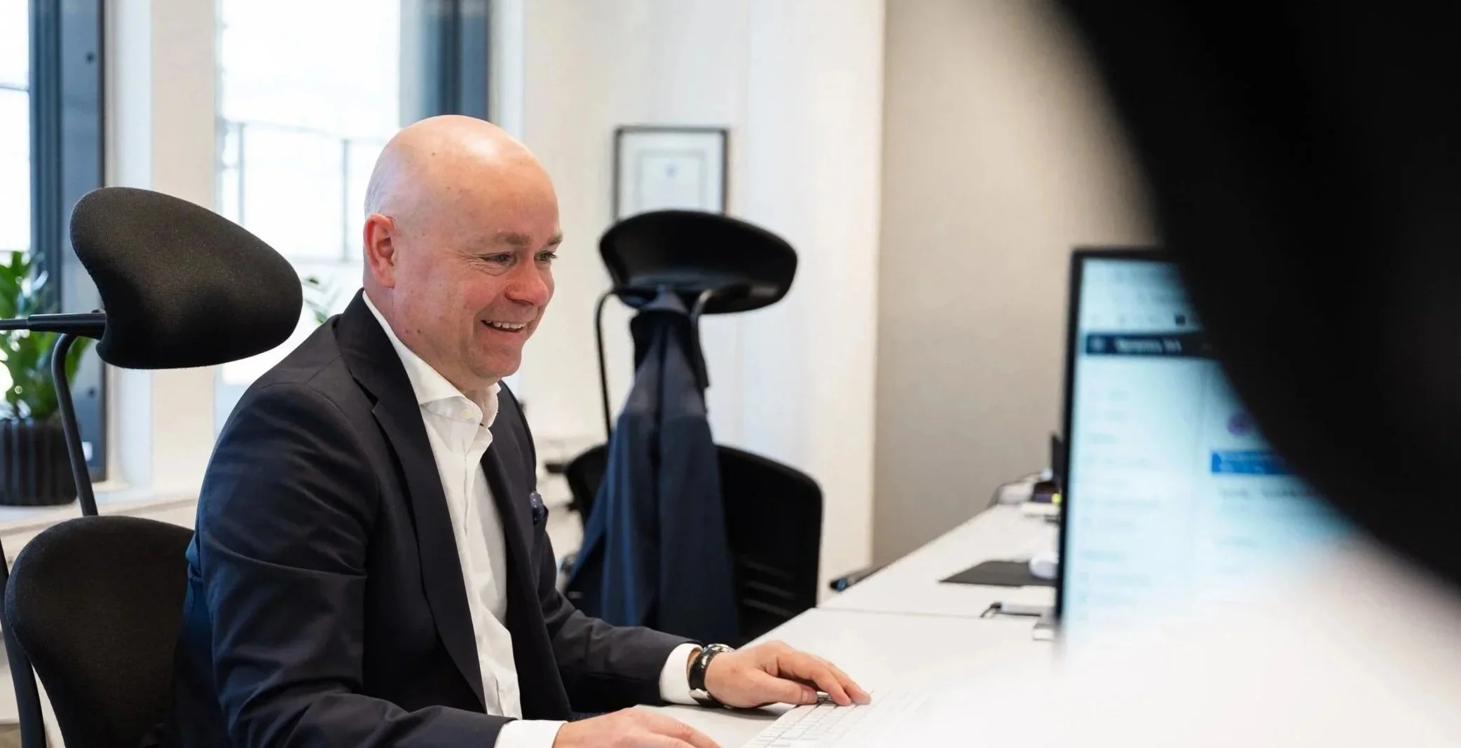 Mann i dress arbeider ved en datamaskin på et kontor.