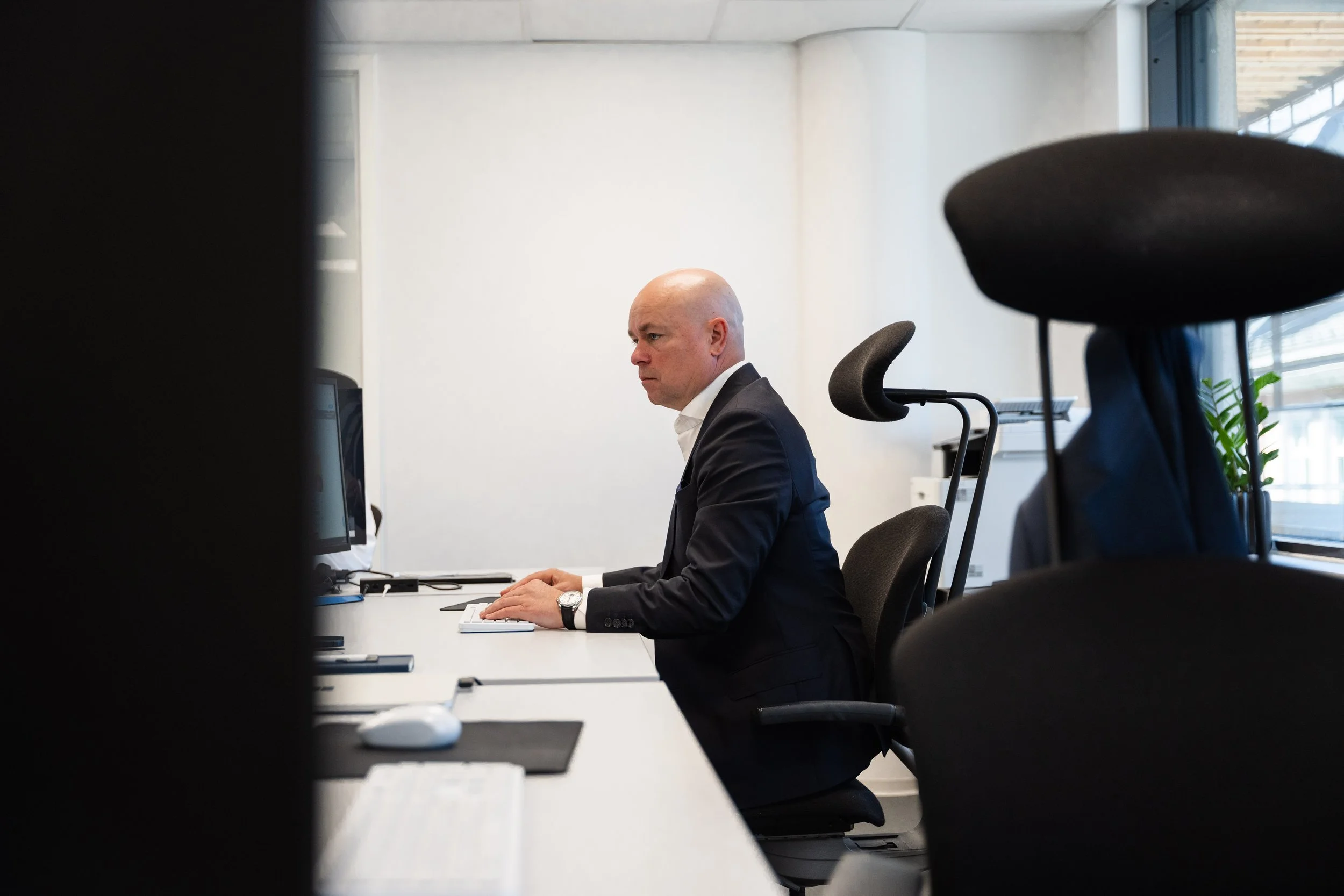 Mann i dress sitter foran en datamaskin på et kontor.