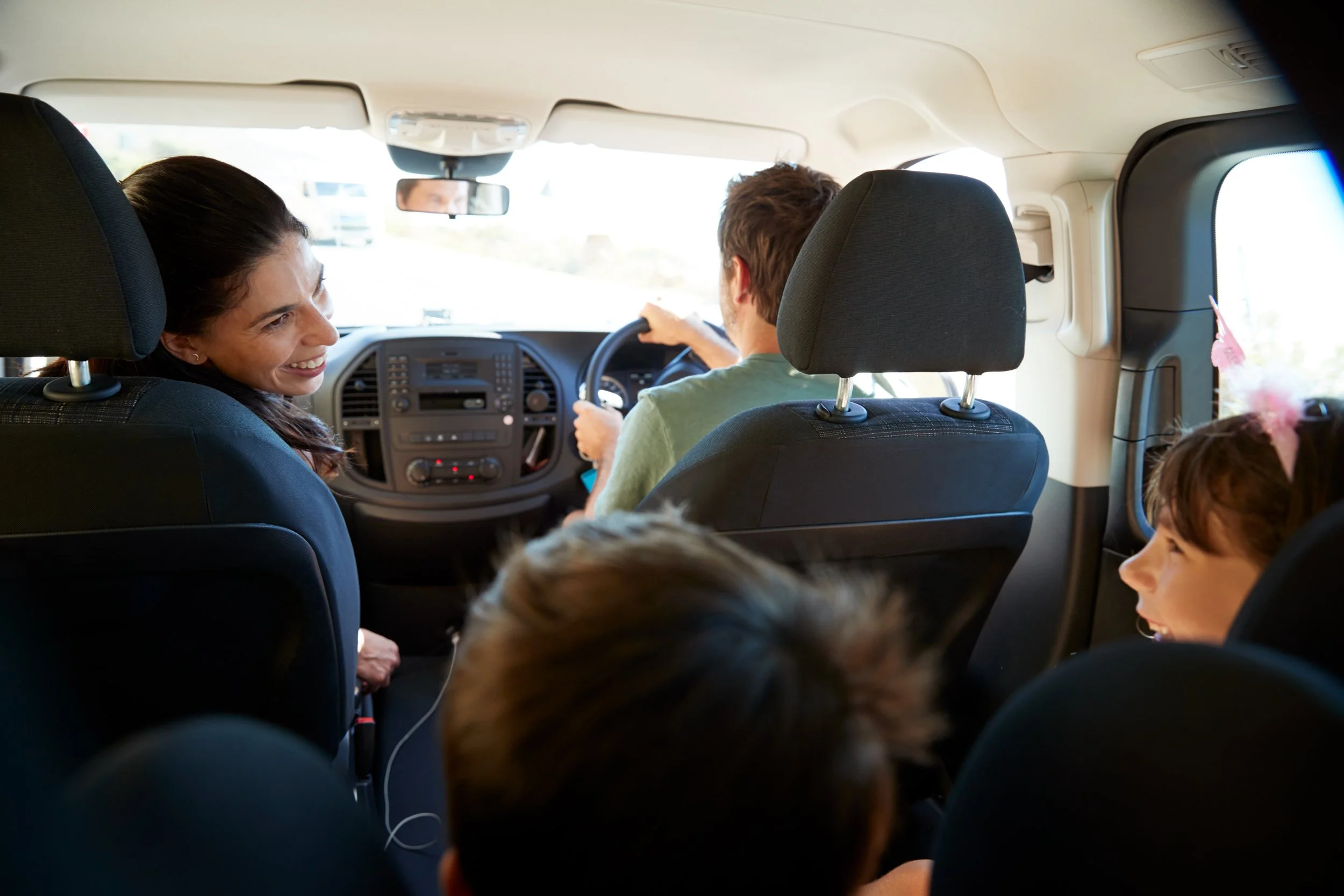 Kent County Council taxi service for schools. Inside a vehicle with passengers, including a woman smiling and a man driving. Children are also visible in the foreground.