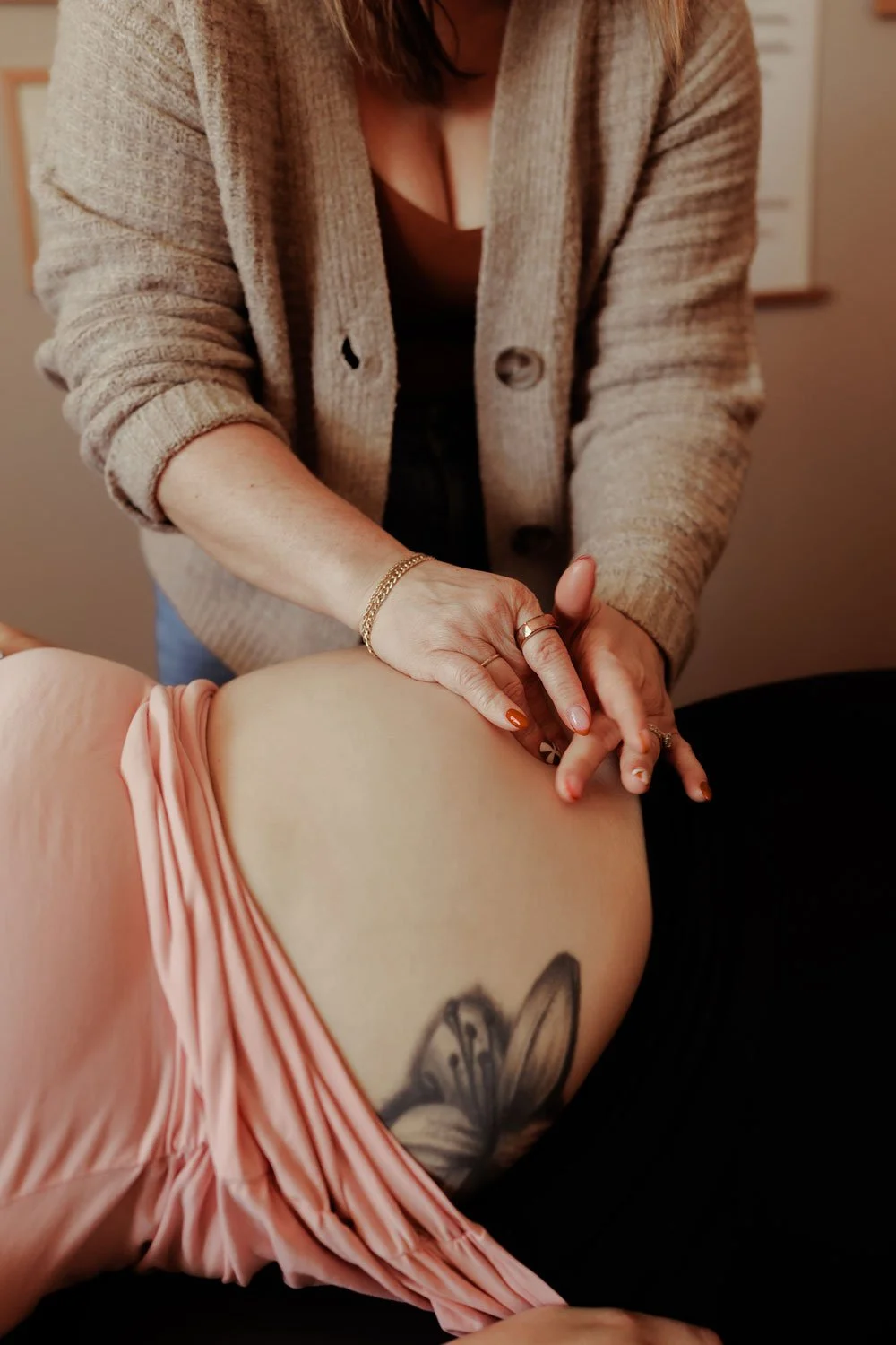 Person giving a massage to another person with a butterfly tattoo on their side, wearing a pink dress and a beige cardigan.