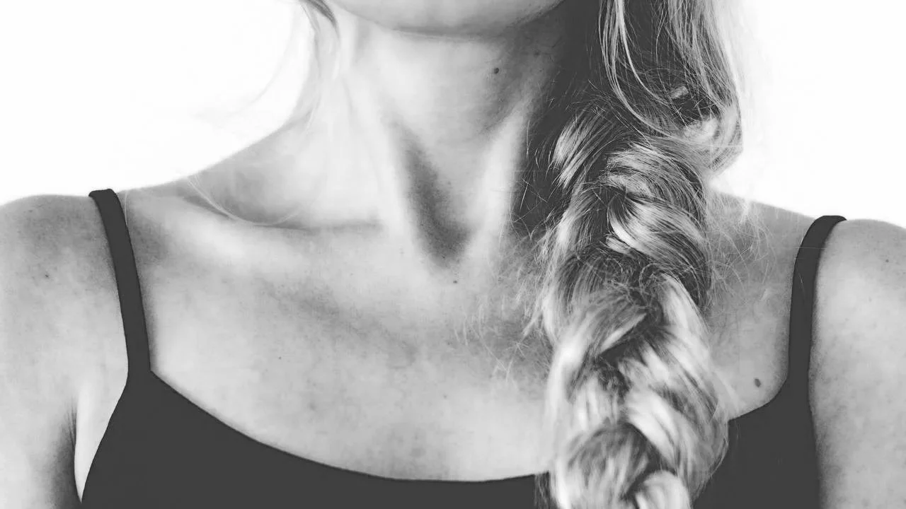 Close-up of a woman's upper body, showing her neck and a side braid hairstyle, wearing a black spaghetti strap top, in black and white.