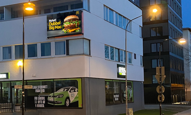 Vy av ett stadshus med reklamskyltar för McDonald's och ett bilföretag, med gator och gatlampor utanför.