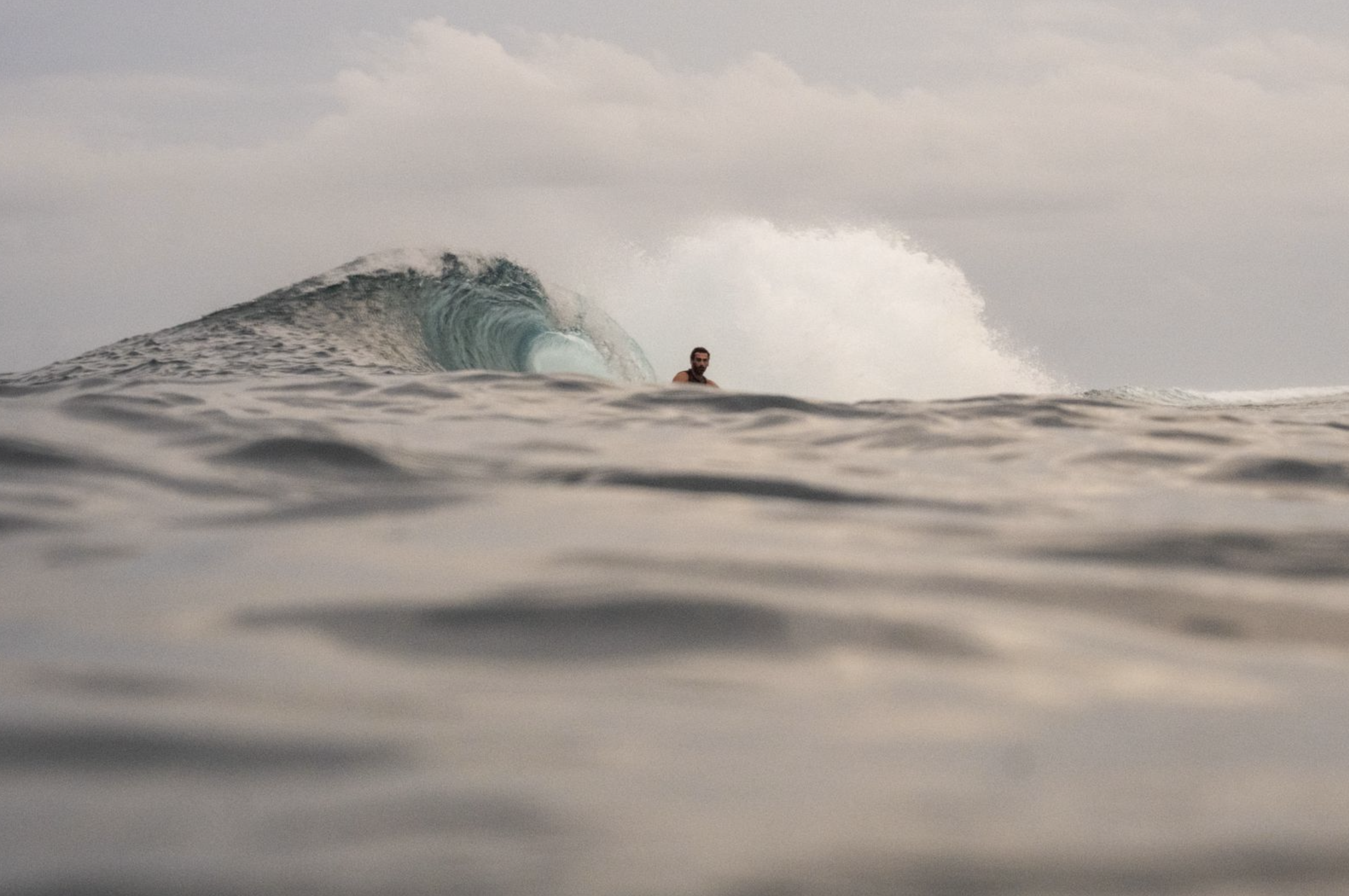 A person surfing on a large wave in the ocean during overcast weather.