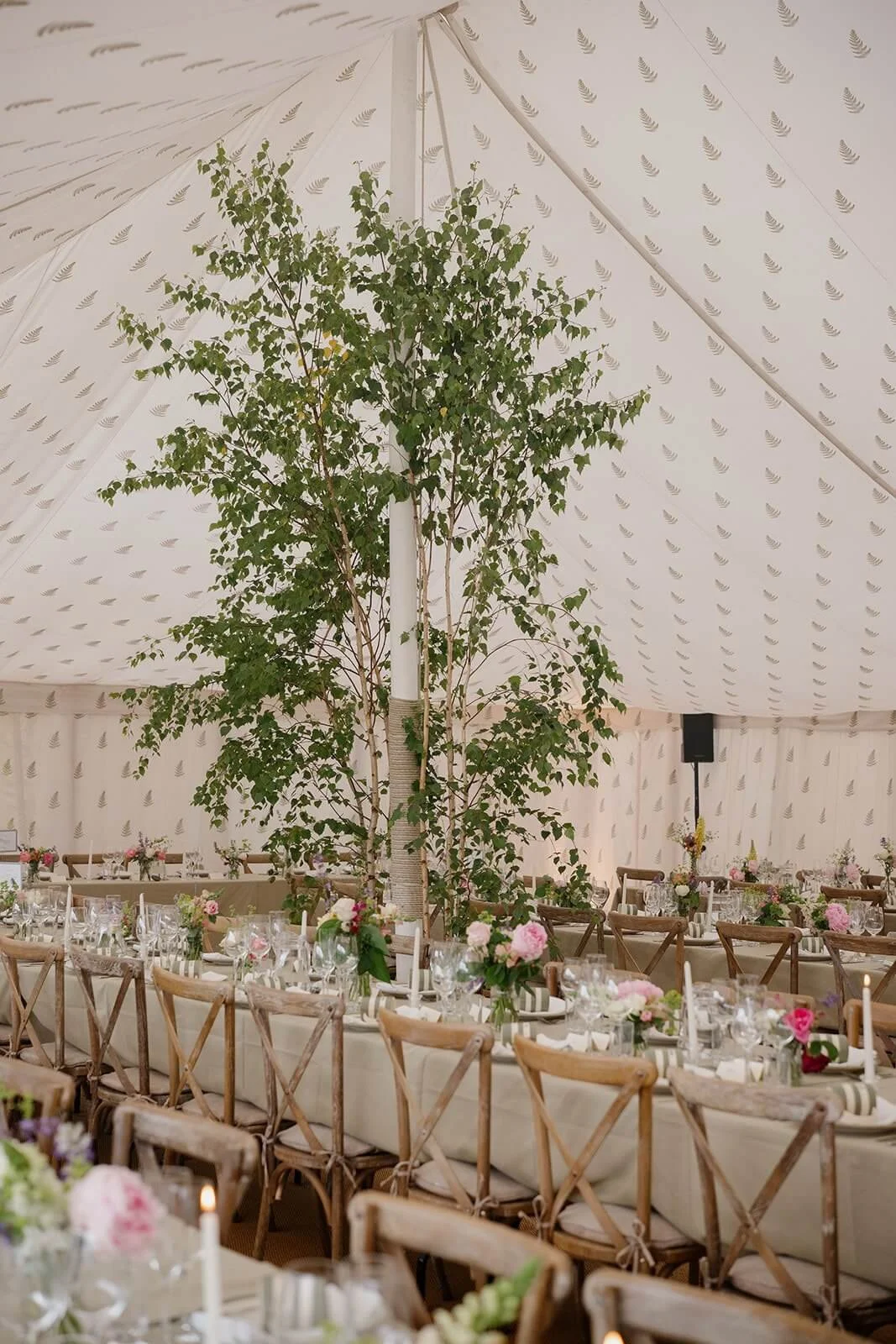Decorated banquet table with wooden chairs, floral centrepieces, candles, and greenery.