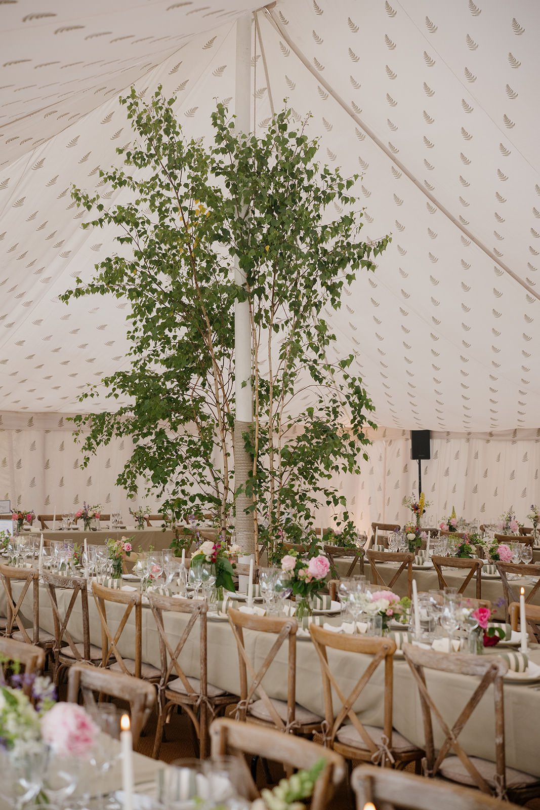 Decorated banquet table with wooden chairs, floral centrepieces, candles, and greenery.