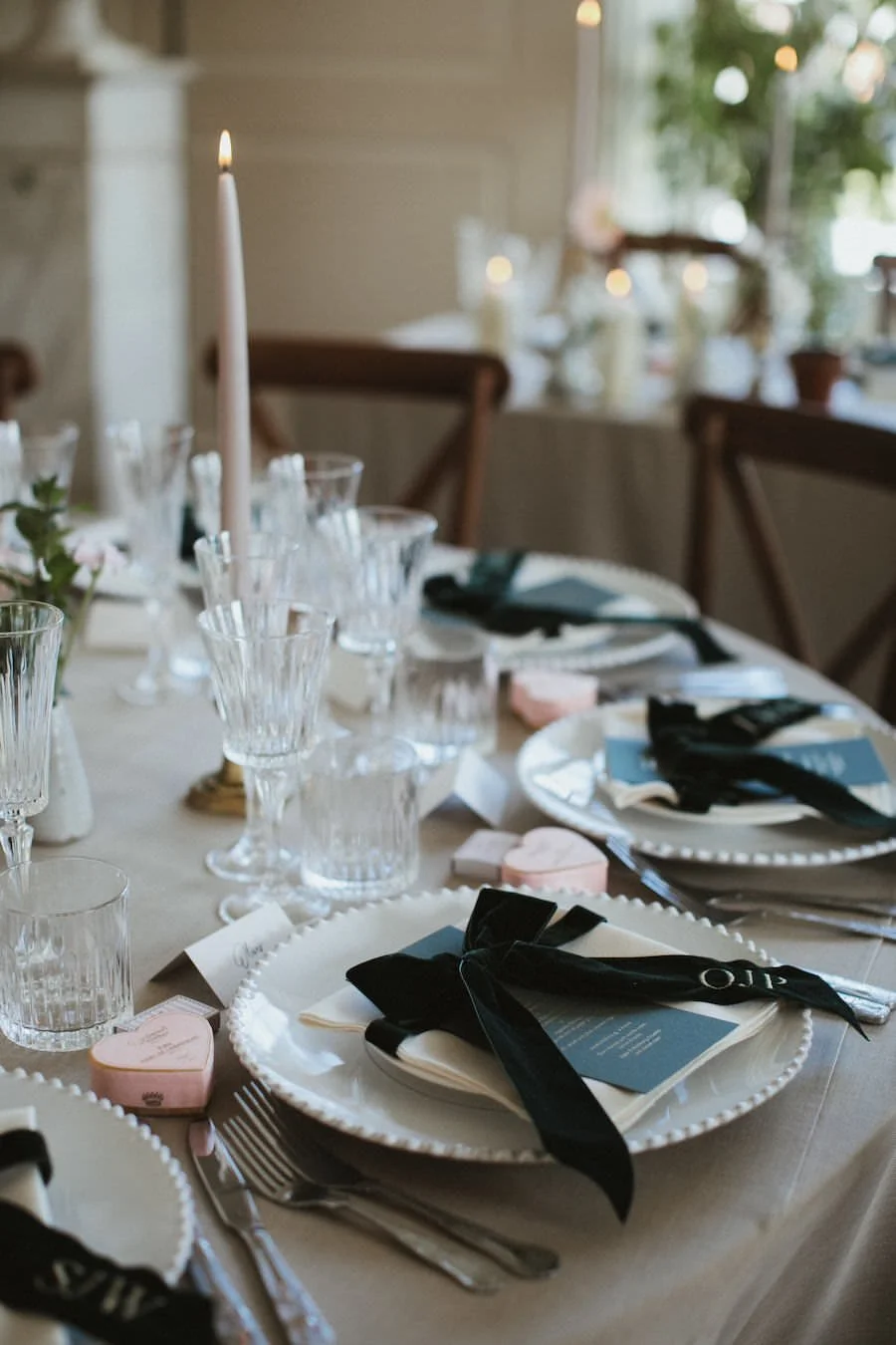 Elegant dining table set with ribbons on napkins, wine glasses, and soft candle lighting, prepared for a special wedding.