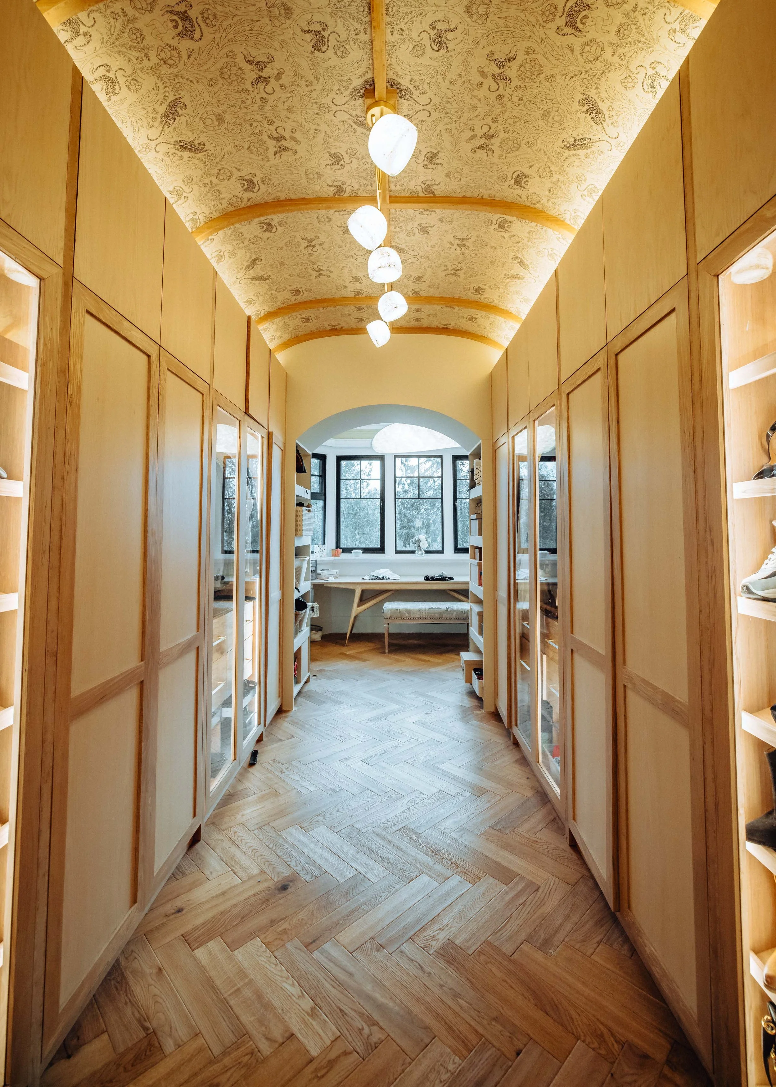 walk in wardrobe made mainly with bamboo, spalted beach doors with glass panels and ash panels, ash faced bamboo boards as top doors, soft mood lighting and an aok floor leading down to a window with a view, by josh hill furniture