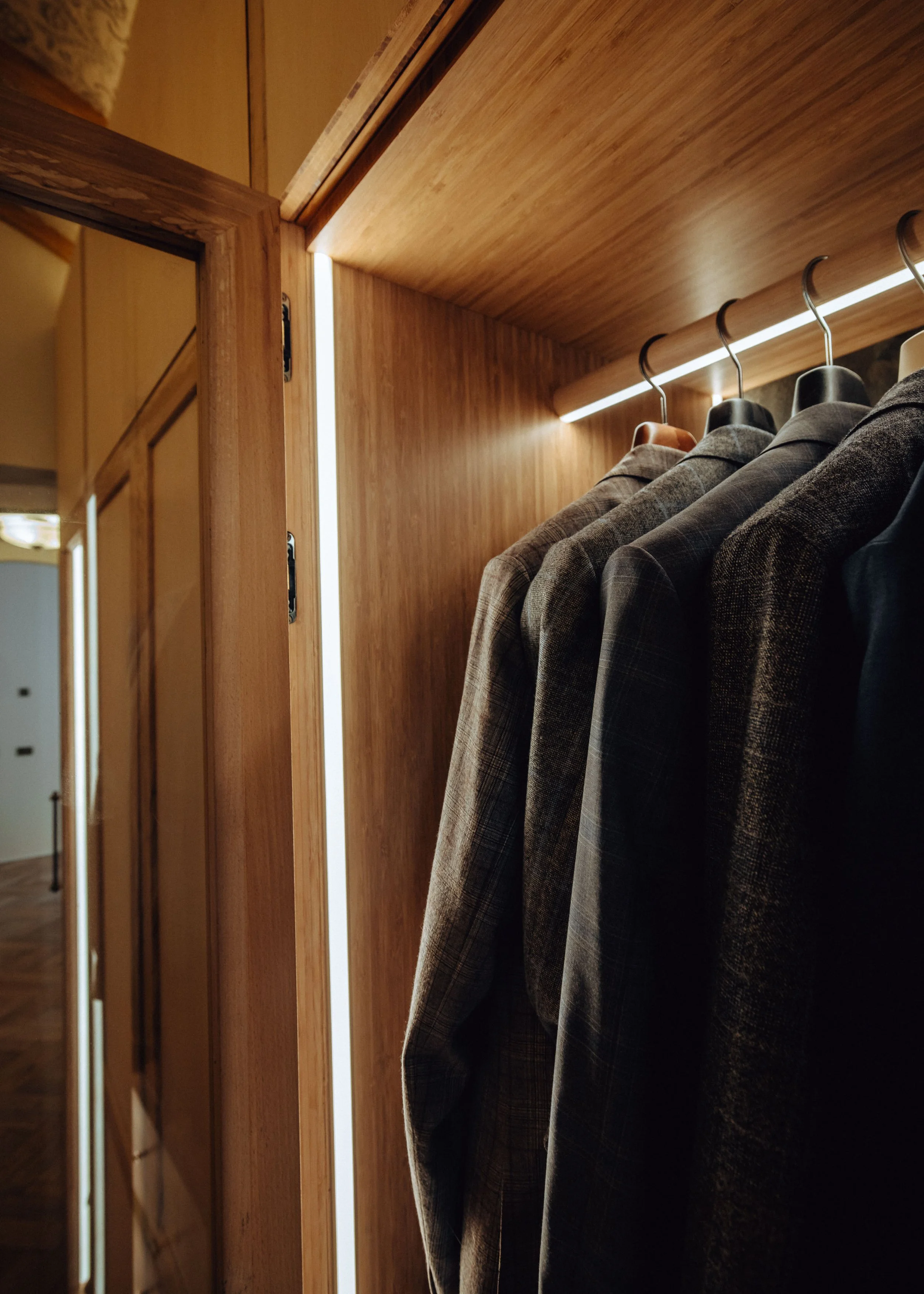 suit jackets in a bamboo wardrobe with spalted beech doors, vertical led strip lights and down lighting in oak hanging rail, by josh hill furniture