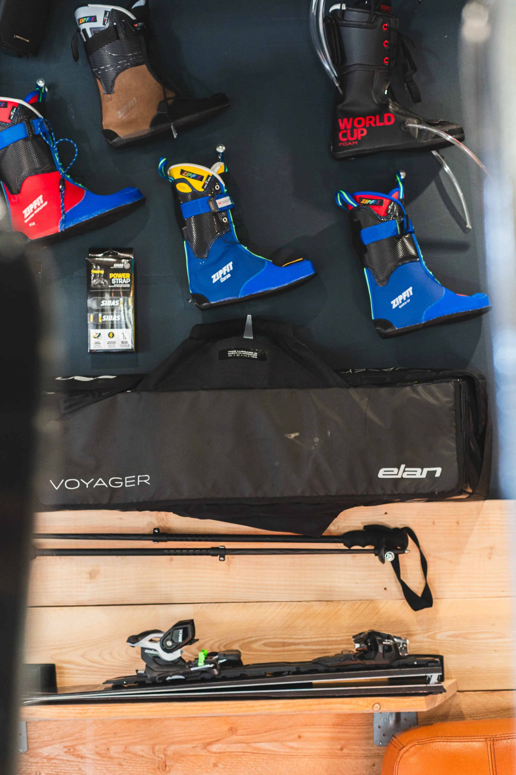 Ski boots, ski poles, a ski bag, and ski bindings arranged on a wooden surface.