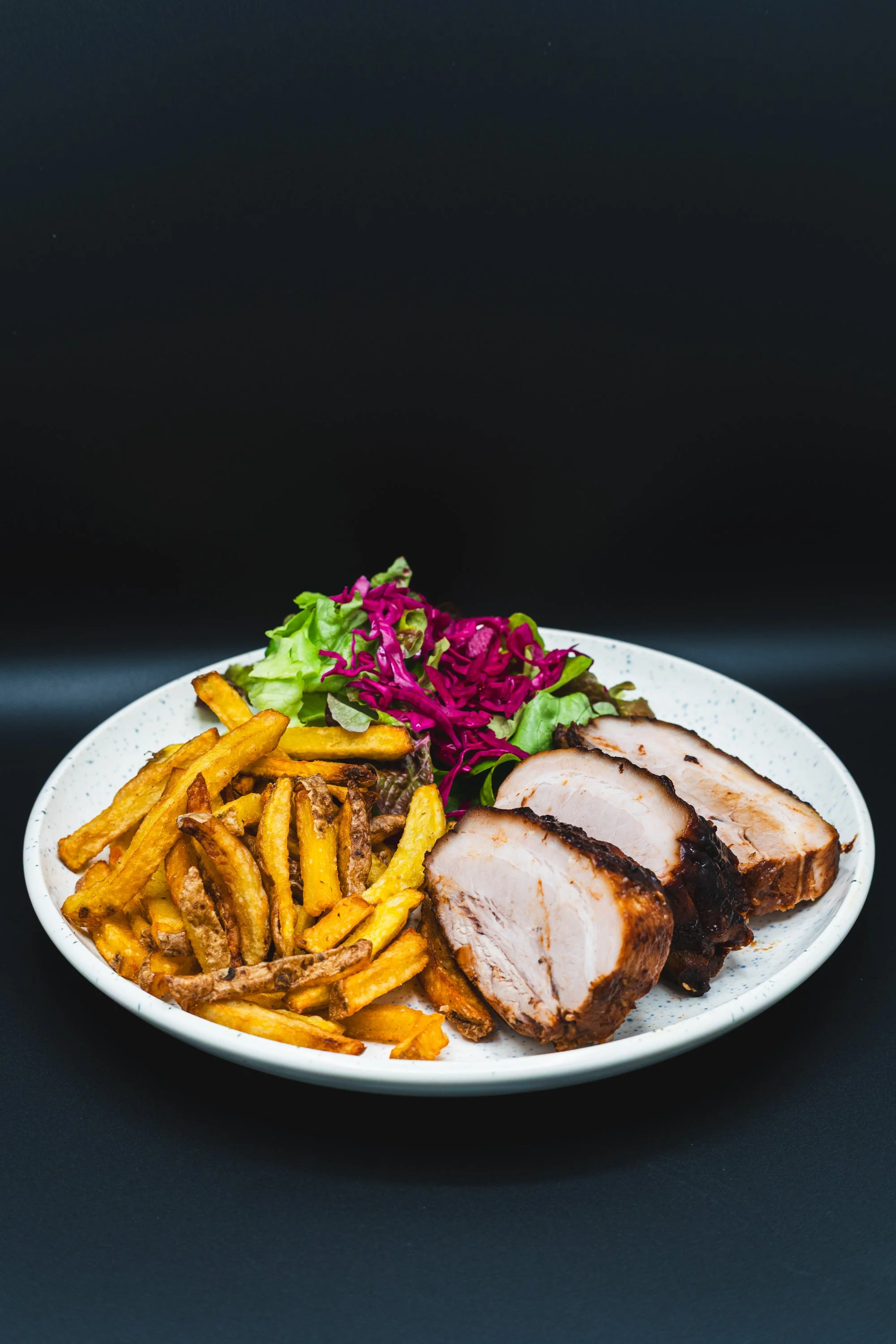 Plate with sliced roasted pork, French fries, and mixed salad with purple cabbage