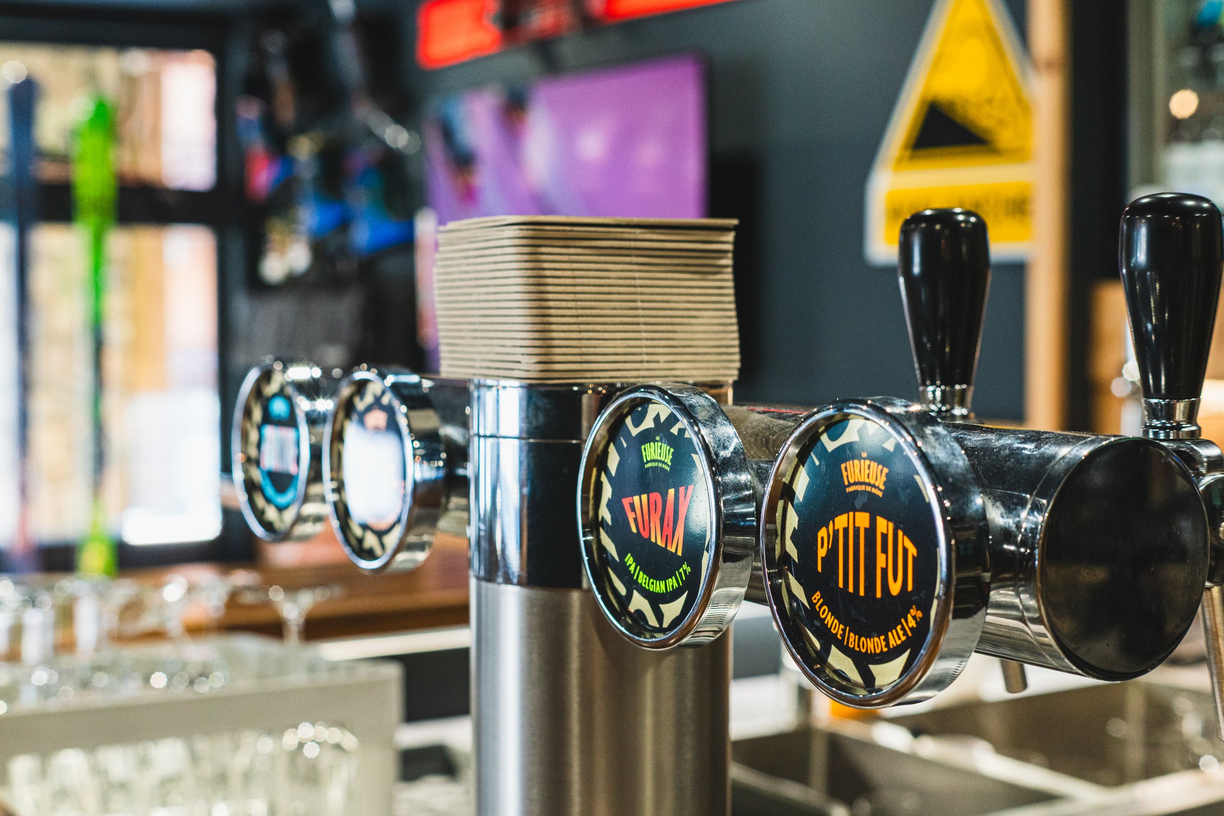 Close-up of a beer tap with two handles on a bar, with a row of beer names and logos on the tap handles.