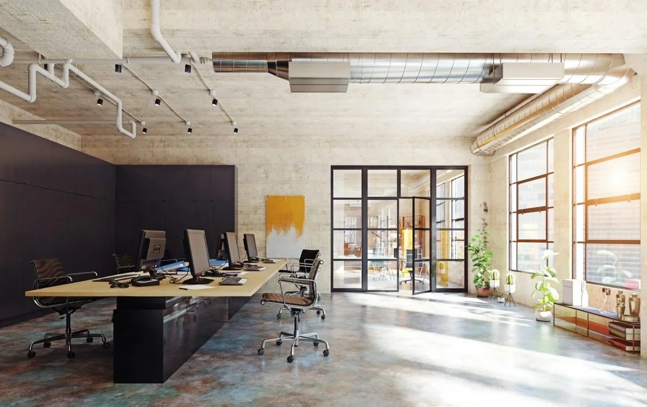 A bright, newly renovated loft office with large windows, desks and plants