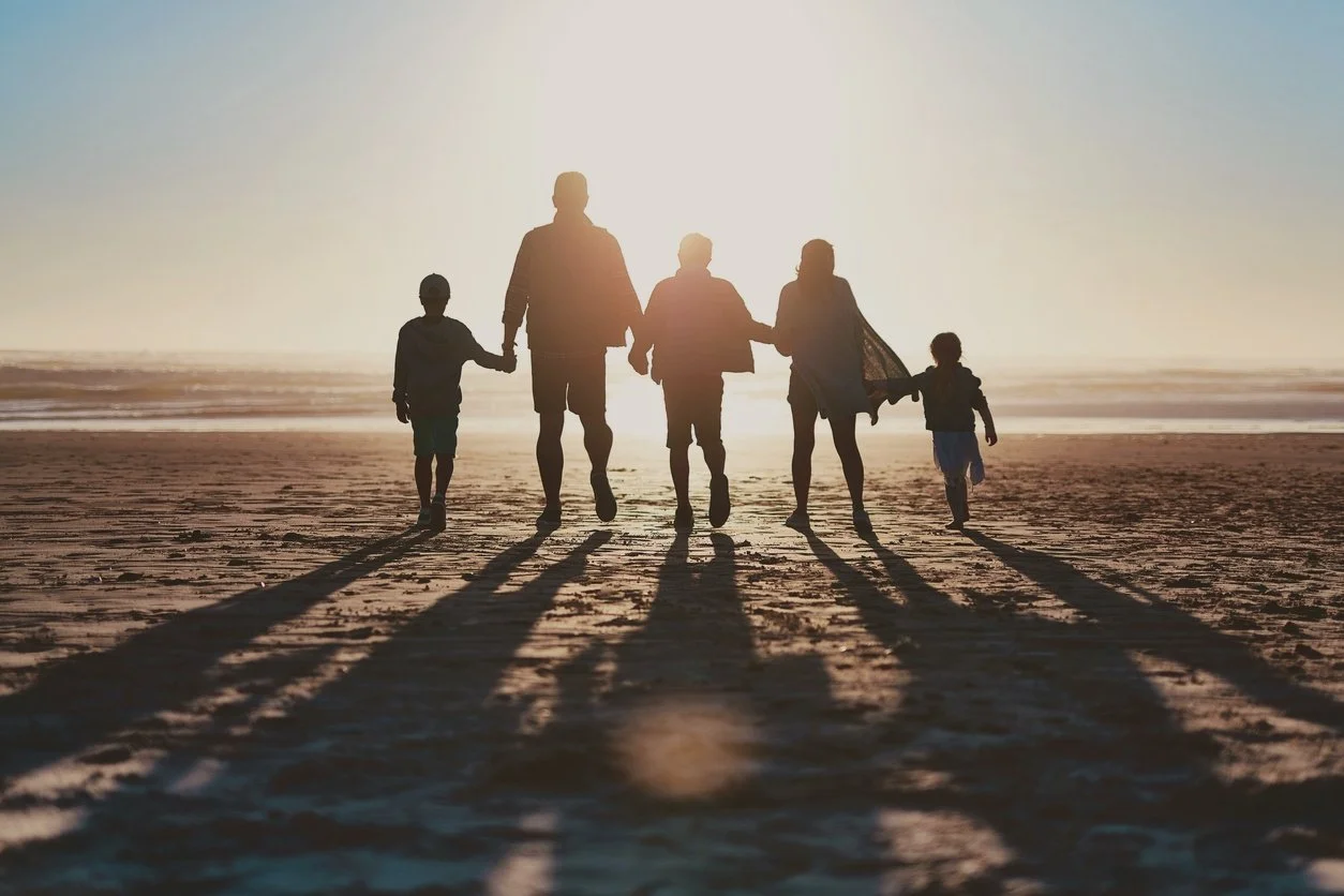 A family holding hands and walking on the beach during sunset, with footprints in the sand and the ocean in the background.