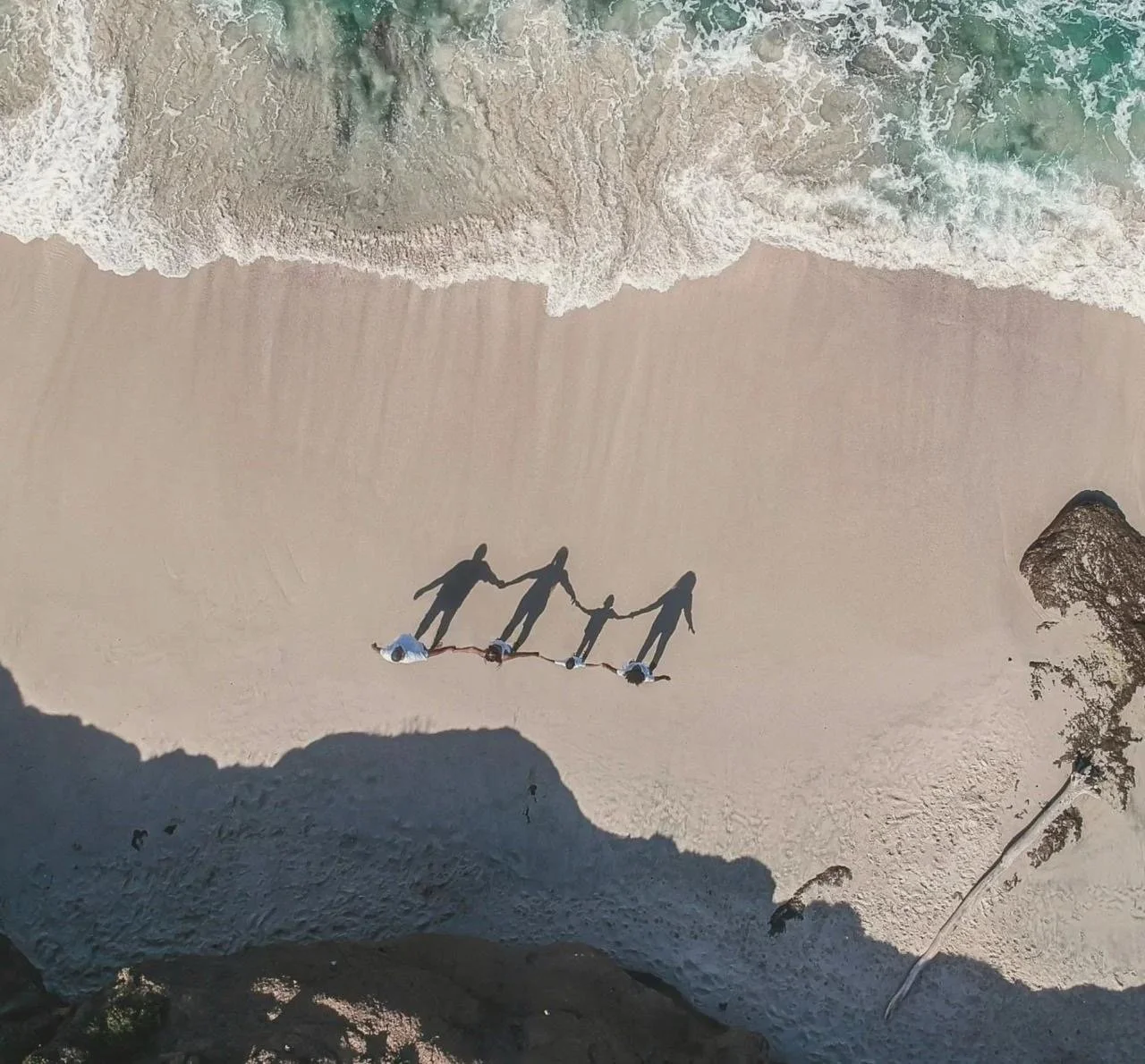 Aerial view of a family of four holding hands on a sandy beach beside the sea