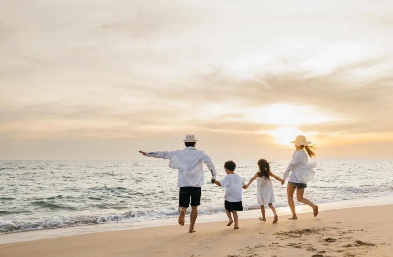 A family of four holding hands and running along a beach at sunset