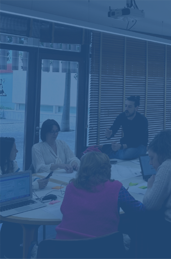 Mentor de Jalea Demente, acompañando a grupo de trabajo en una sala con varias personas sentadas alrededor de una mesa en un Hackaton en Mallorca