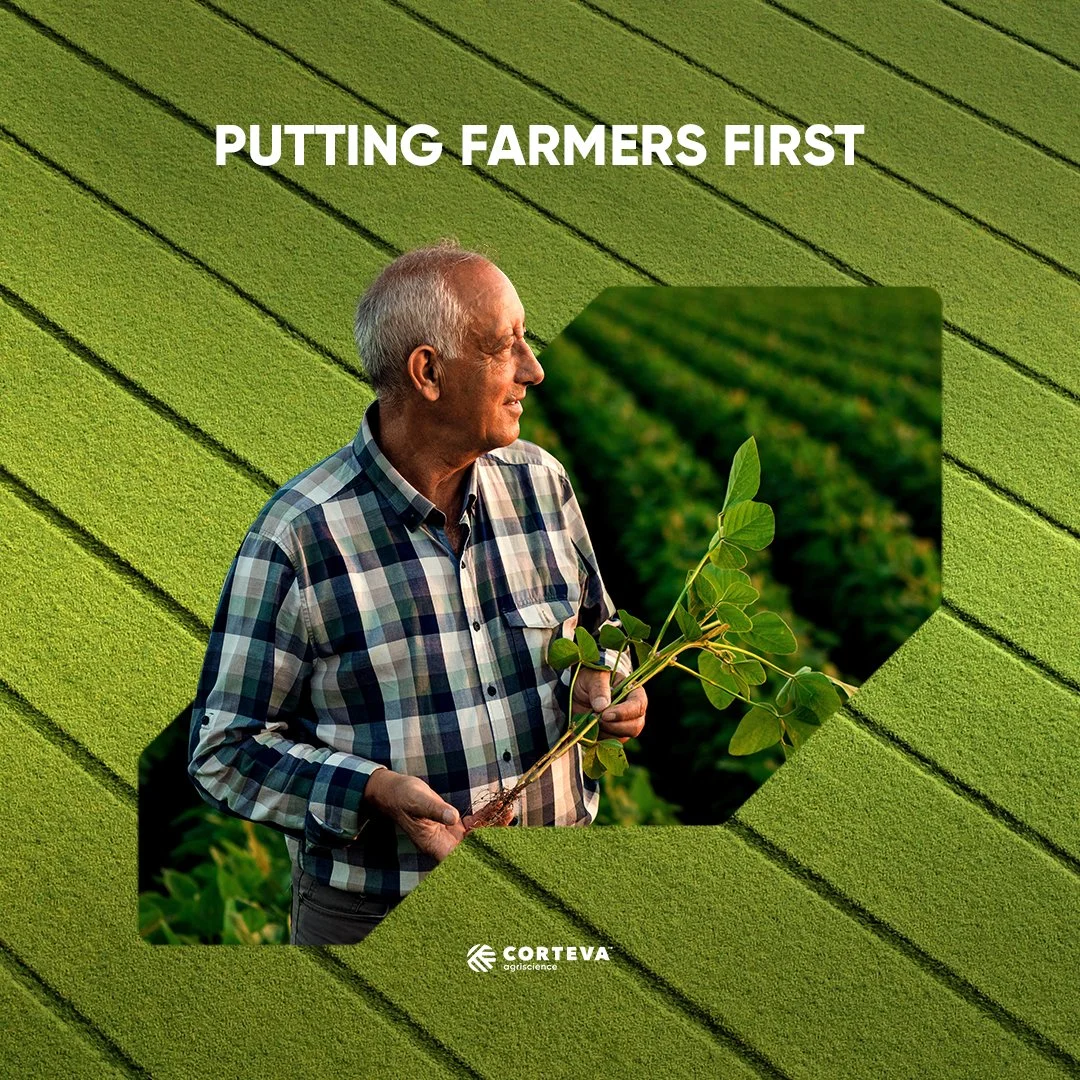 Man in checkered shirt holding a young plant in a field of crops with green rows, with the phrase "Putting Farmers First" at the top.