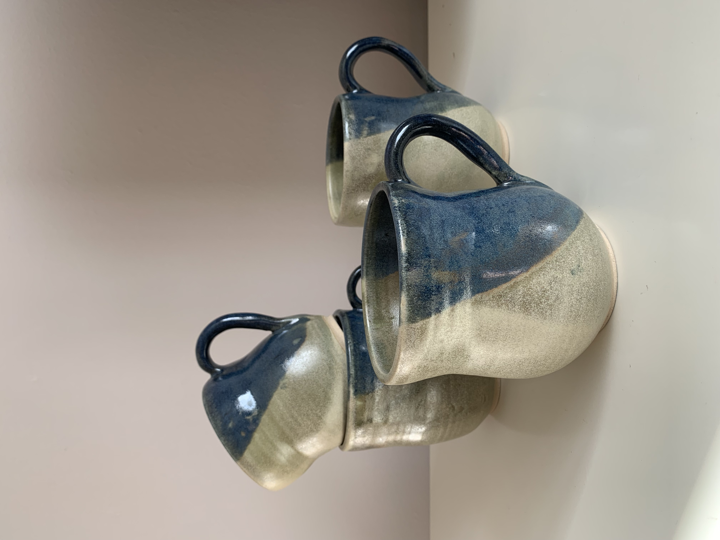 Three ceramic coffee mugs with a blue and beige two-tone glaze, arranged on a white surface against a plain background.