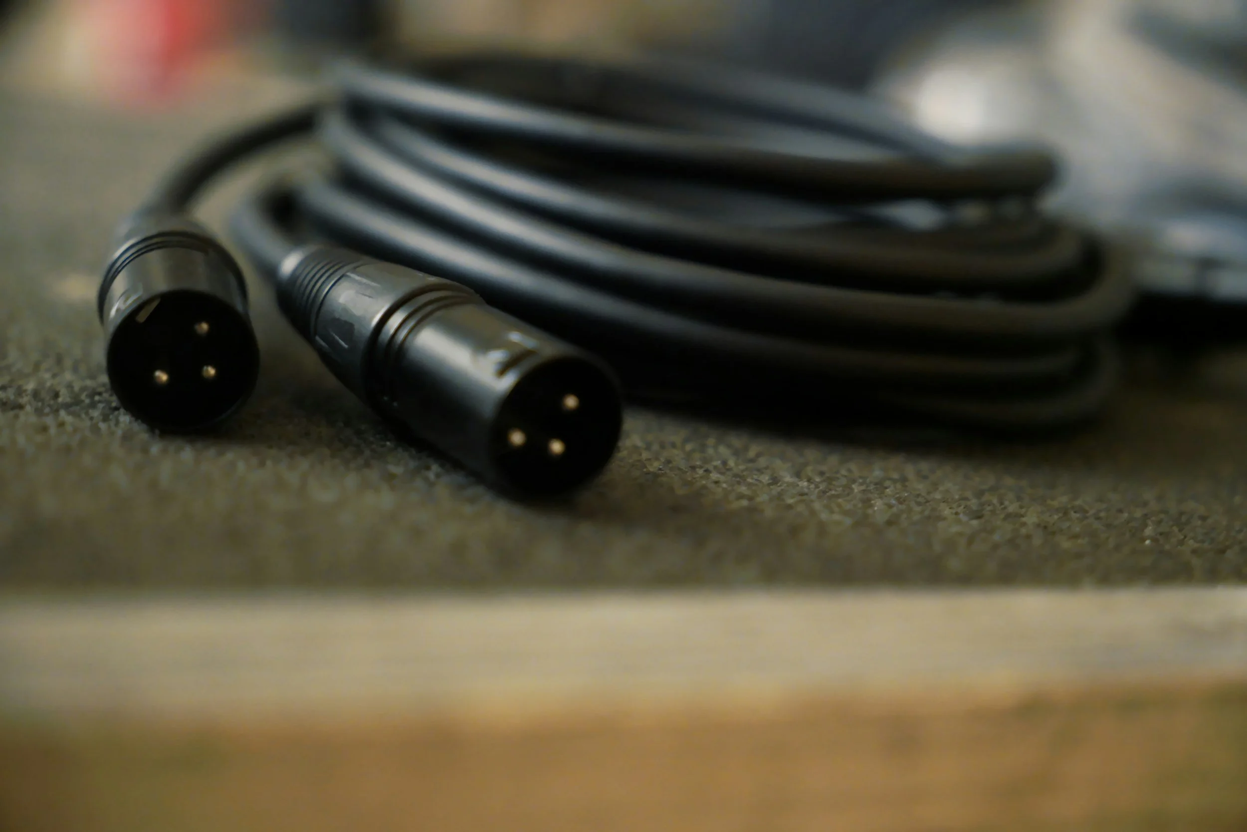 A black audio cable with male XLR connectors on both ends, coiled on a gray surface.