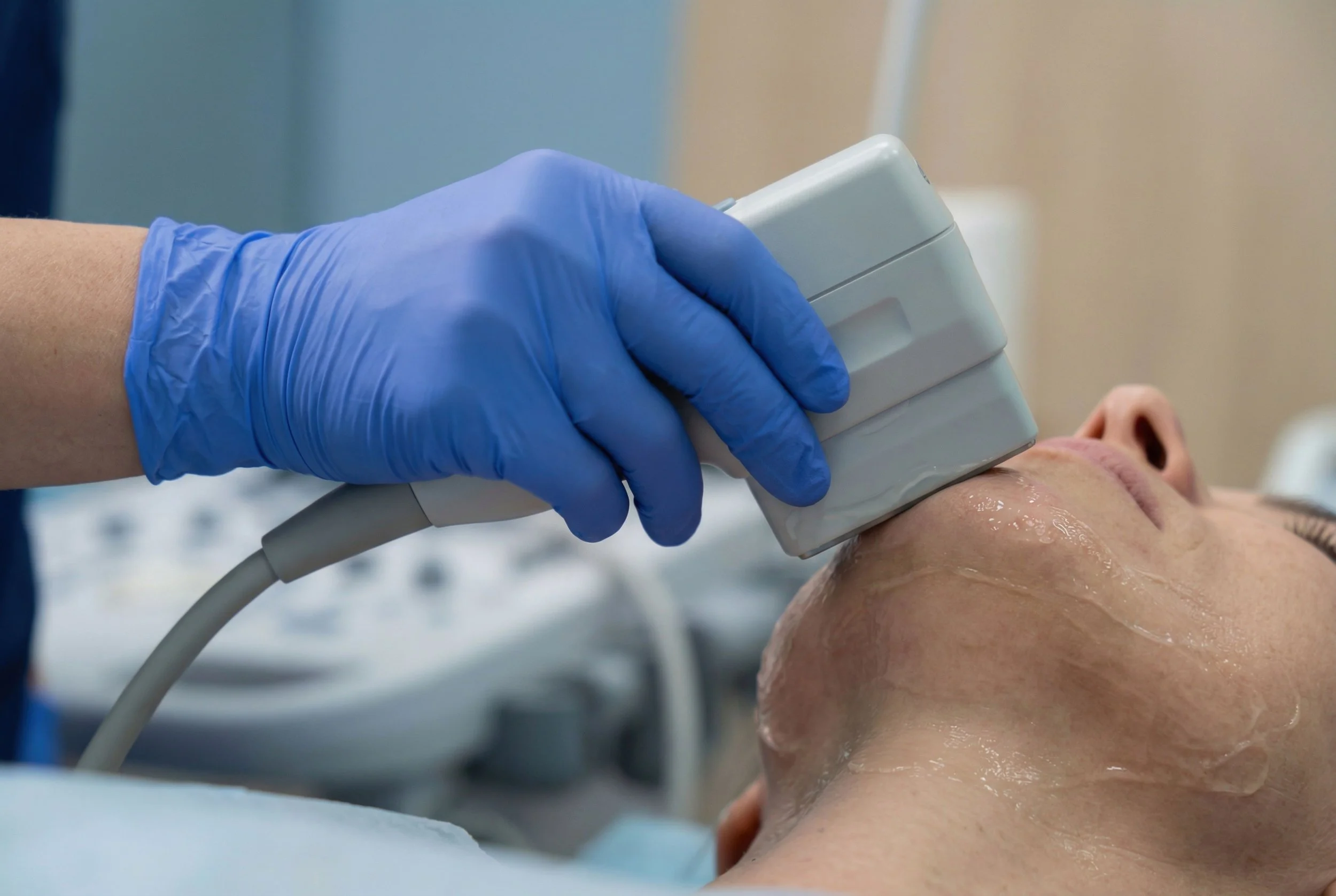 Une personne reçoit un examen médical avec un appareil à ultrasons sur la joue, tenue par un professionnel avec des gants bleus.