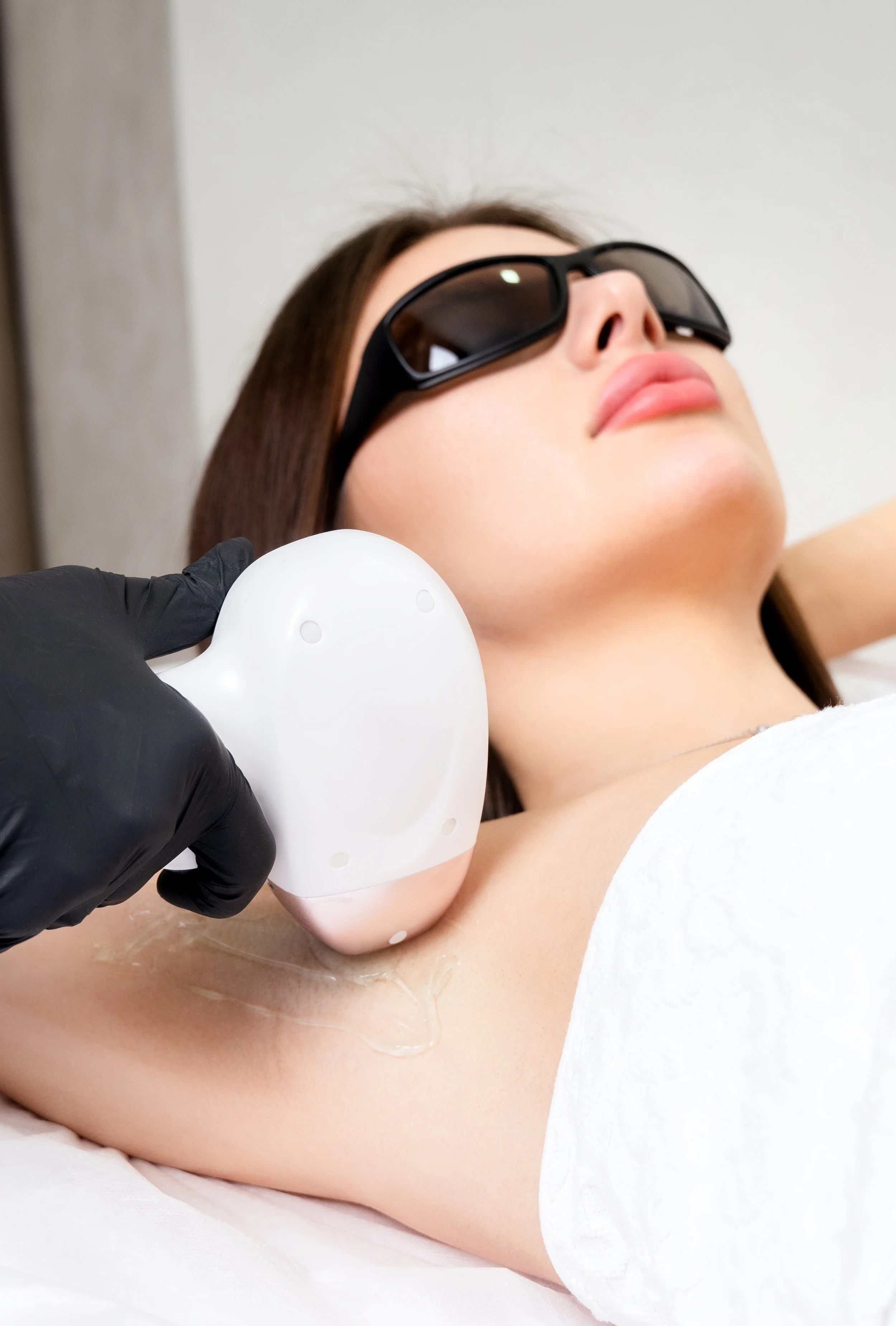 Une femme portant des lunettes de soleil reçoit un traitement de radiofréquence sur le cou, administré par un professionnel portant des gants noirs.