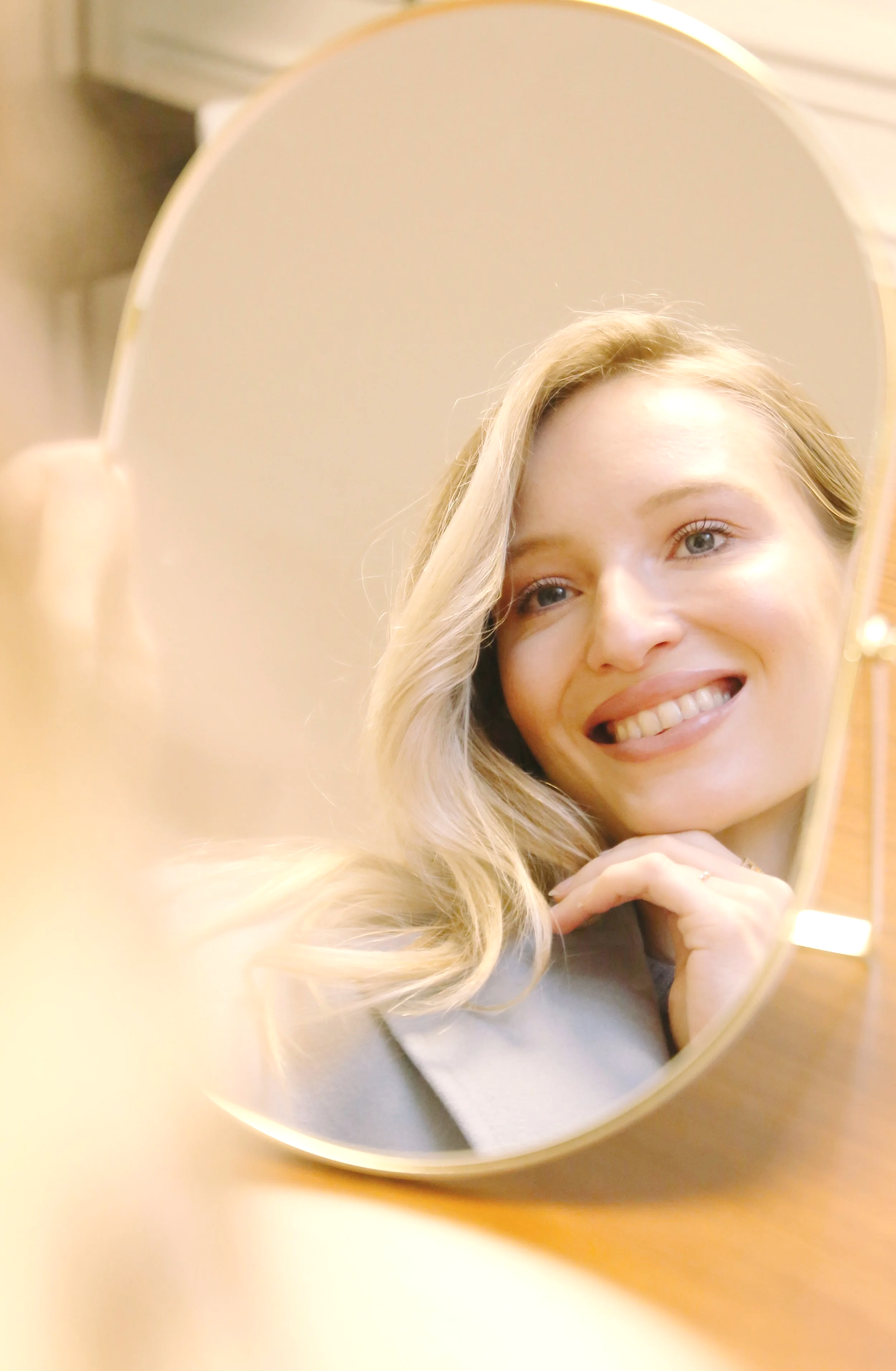 Une femme regarde son reflet dans un miroir rond en train de sourire.