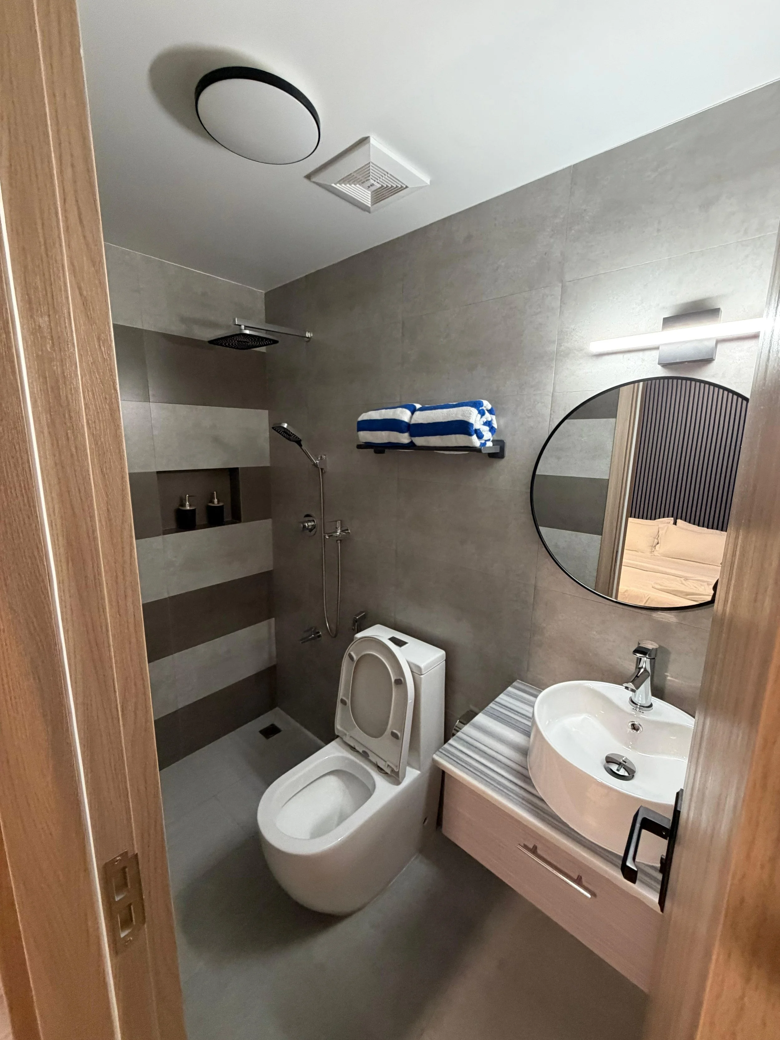 Modern bathroom with toilet, sink, mirror, towels, and walk-in shower with rain showerhead.