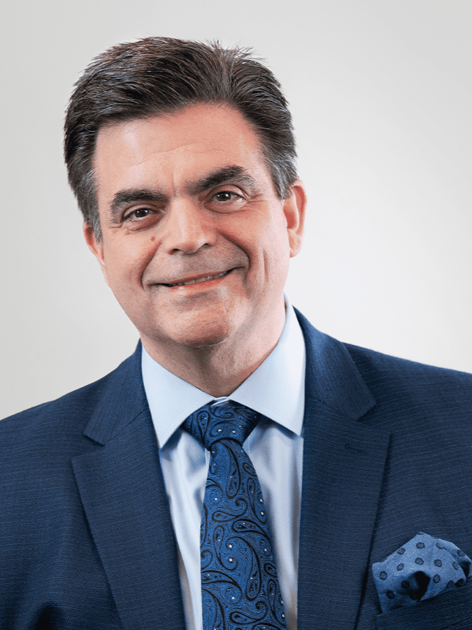Portrait of a middle-aged man in a navy suit and blue patterned tie, smiling slightly against a plain white background.
