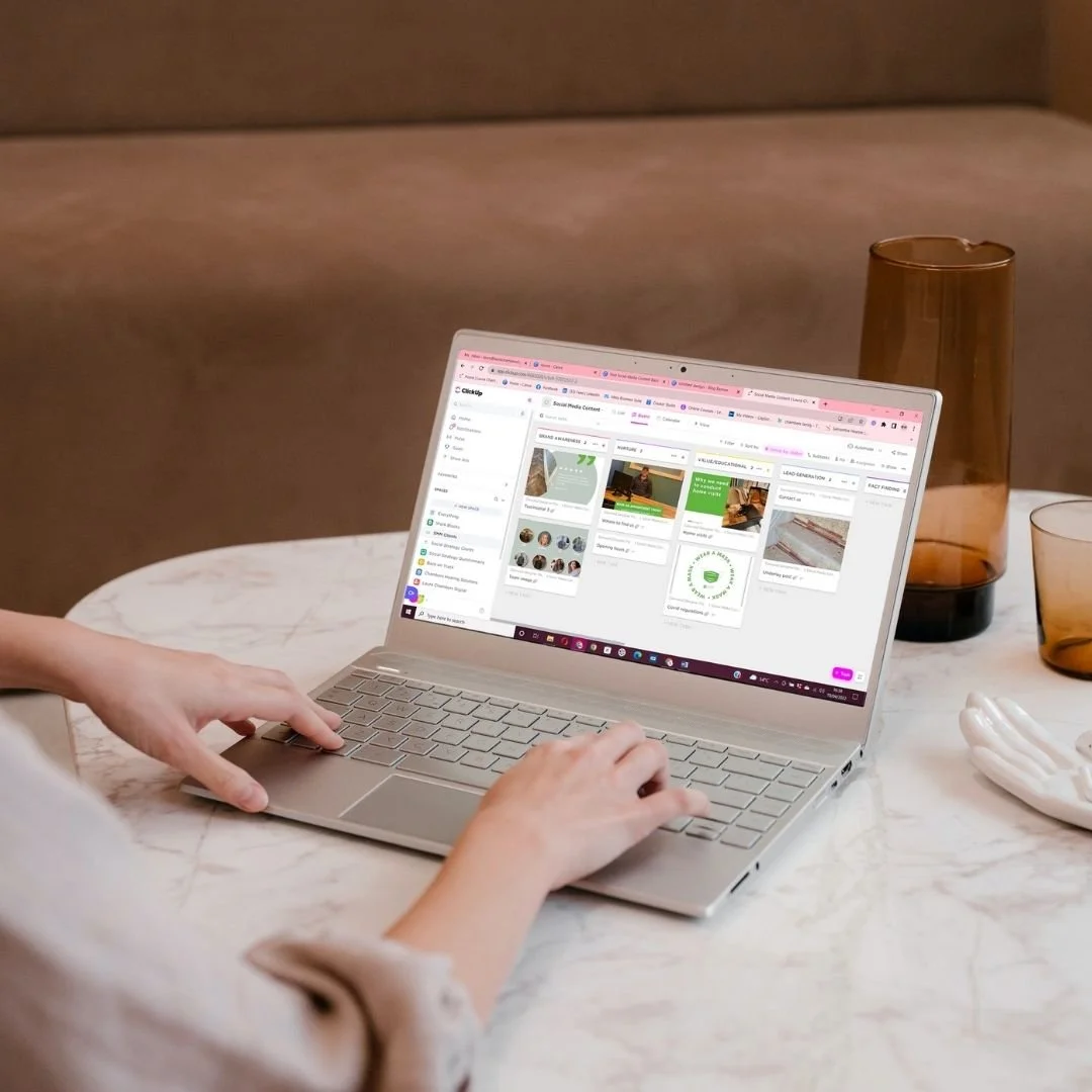 Laptop displaying a social media management dashboard on a marble table with brown vases and glasses.