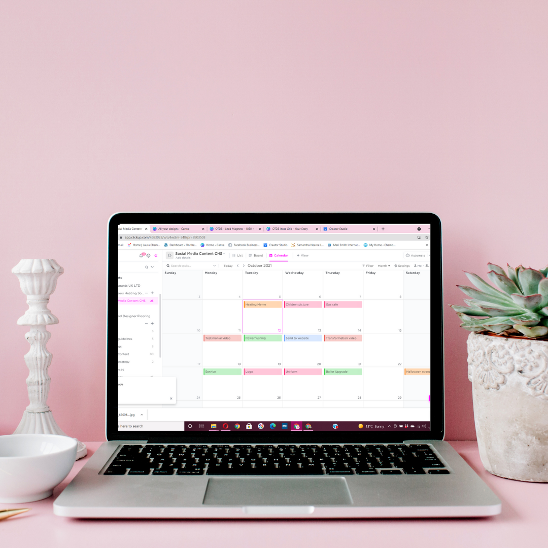 Laptop on a pink desk displaying a social media content calendar, flanked by a white candle holder and a potted succulent plant.