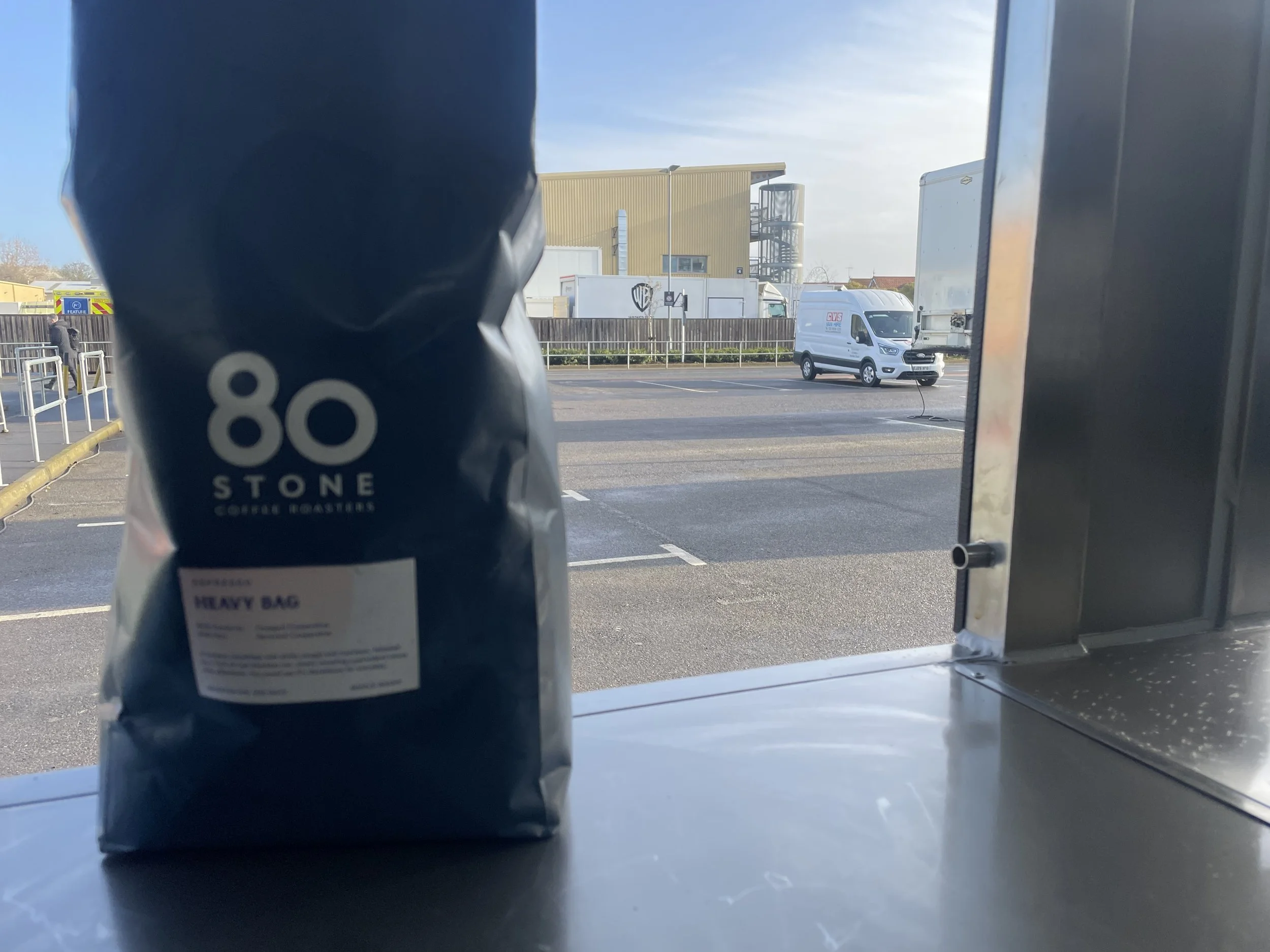 A bag of coffee beans labeled '80 Stone Coffee Roasters' placed on a counter near a window with a view of a parking lot and moving trucks outside.