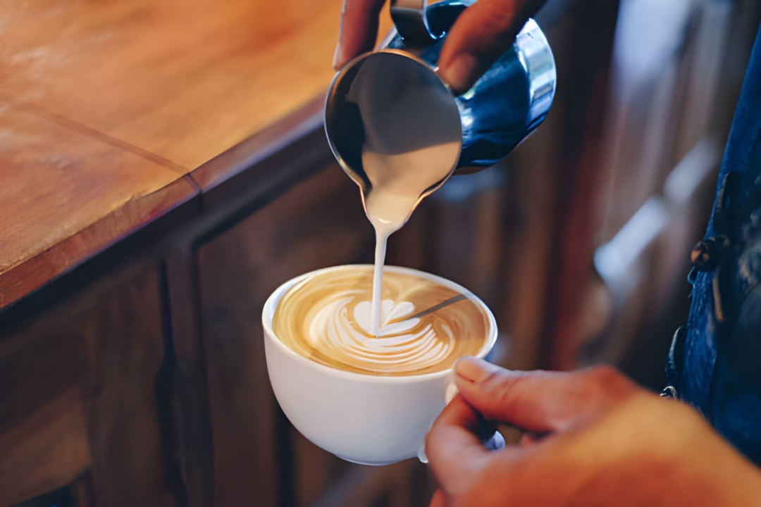 Person pouring steamed milk into a cup of coffee to create latte art.