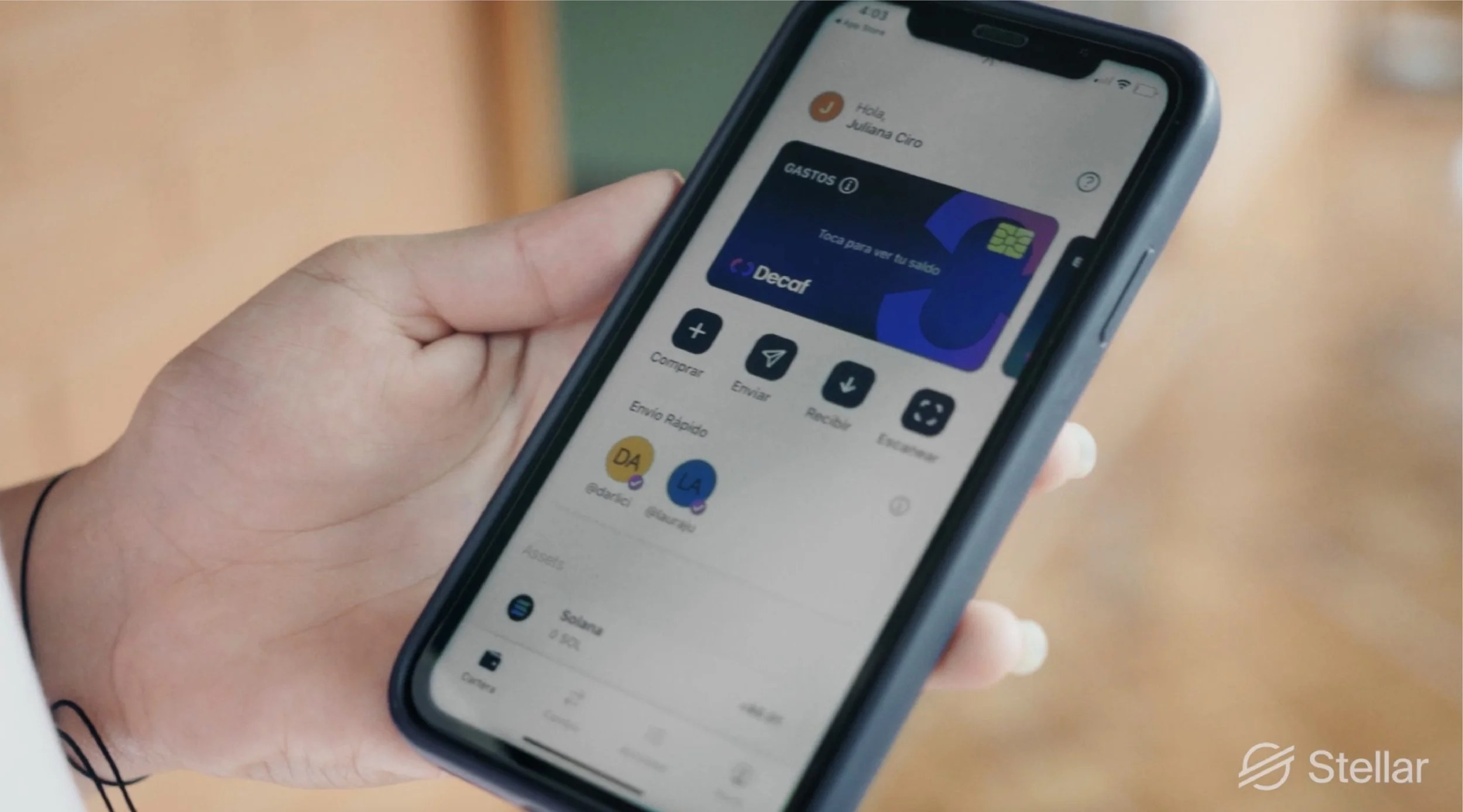 A person holding a smartphone displaying a financial app with a virtual card labeled 'Decaf' and options for sharing, sending, and other functions.