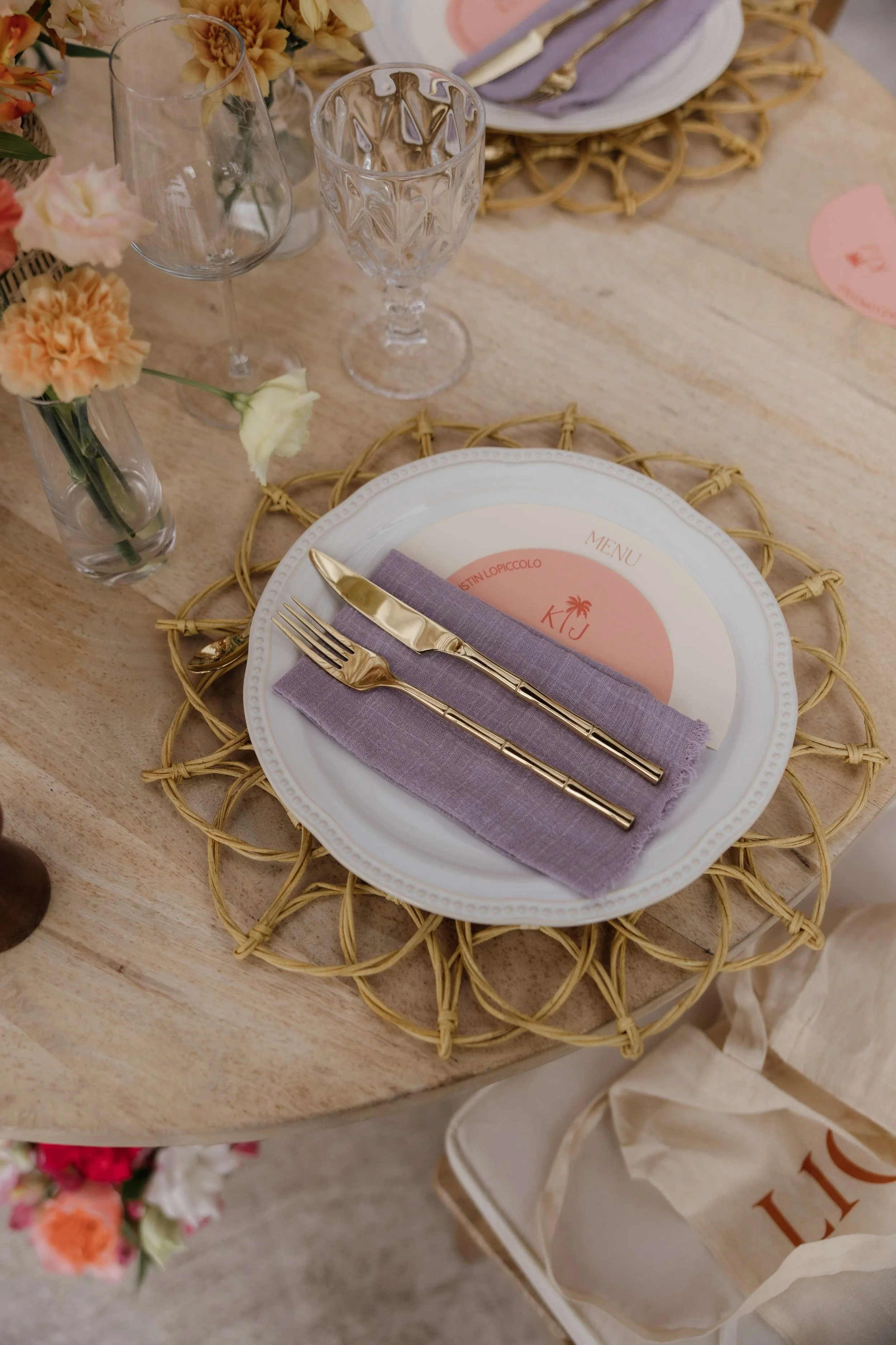 Table setting with a white plate, purple cloth napkin, gold utensils, a menu card, and floral centerpiece at a dining table.