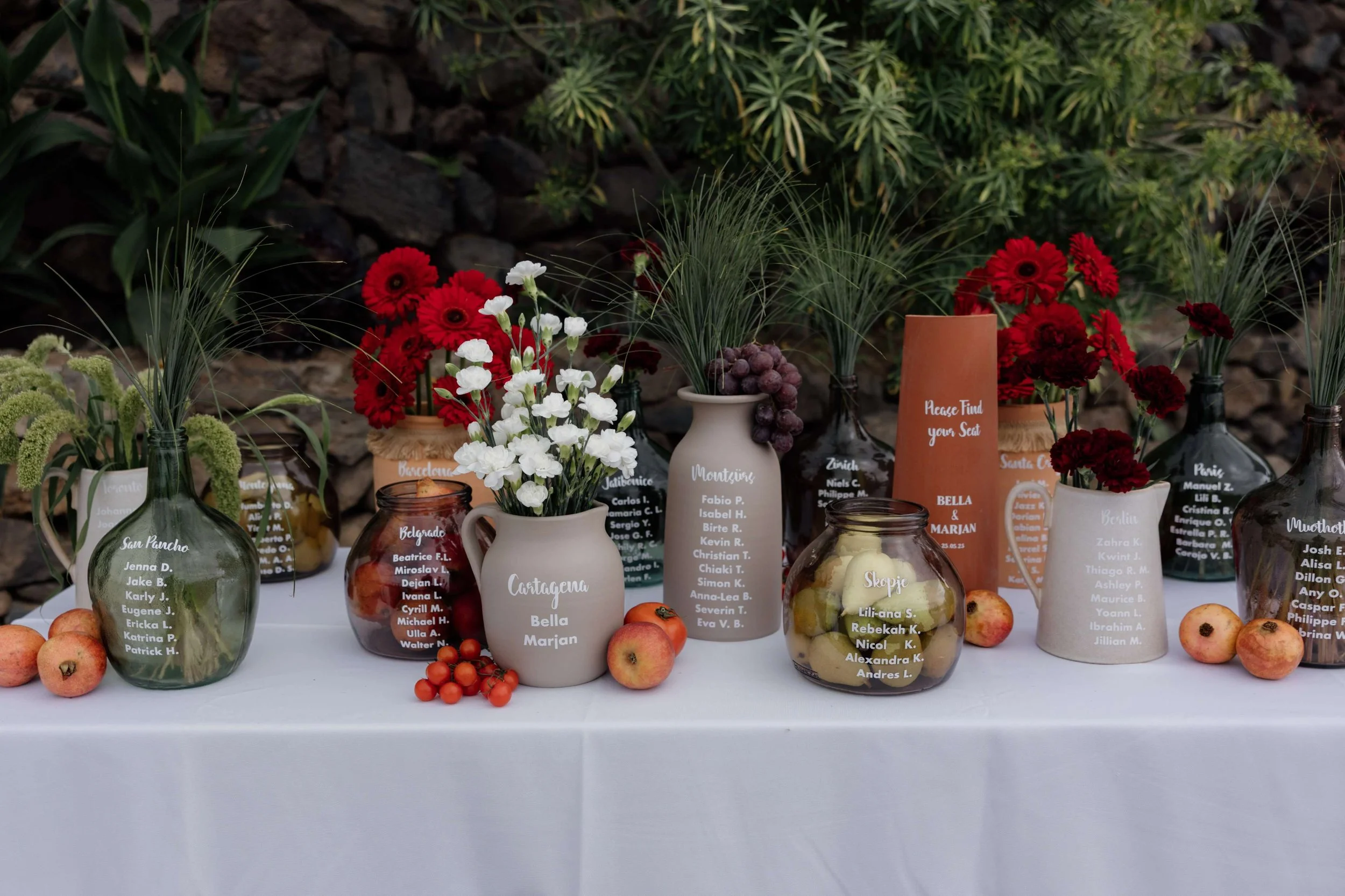 Table decorated with various vases containing flowers, fruit, and handwritten name tags for guests
