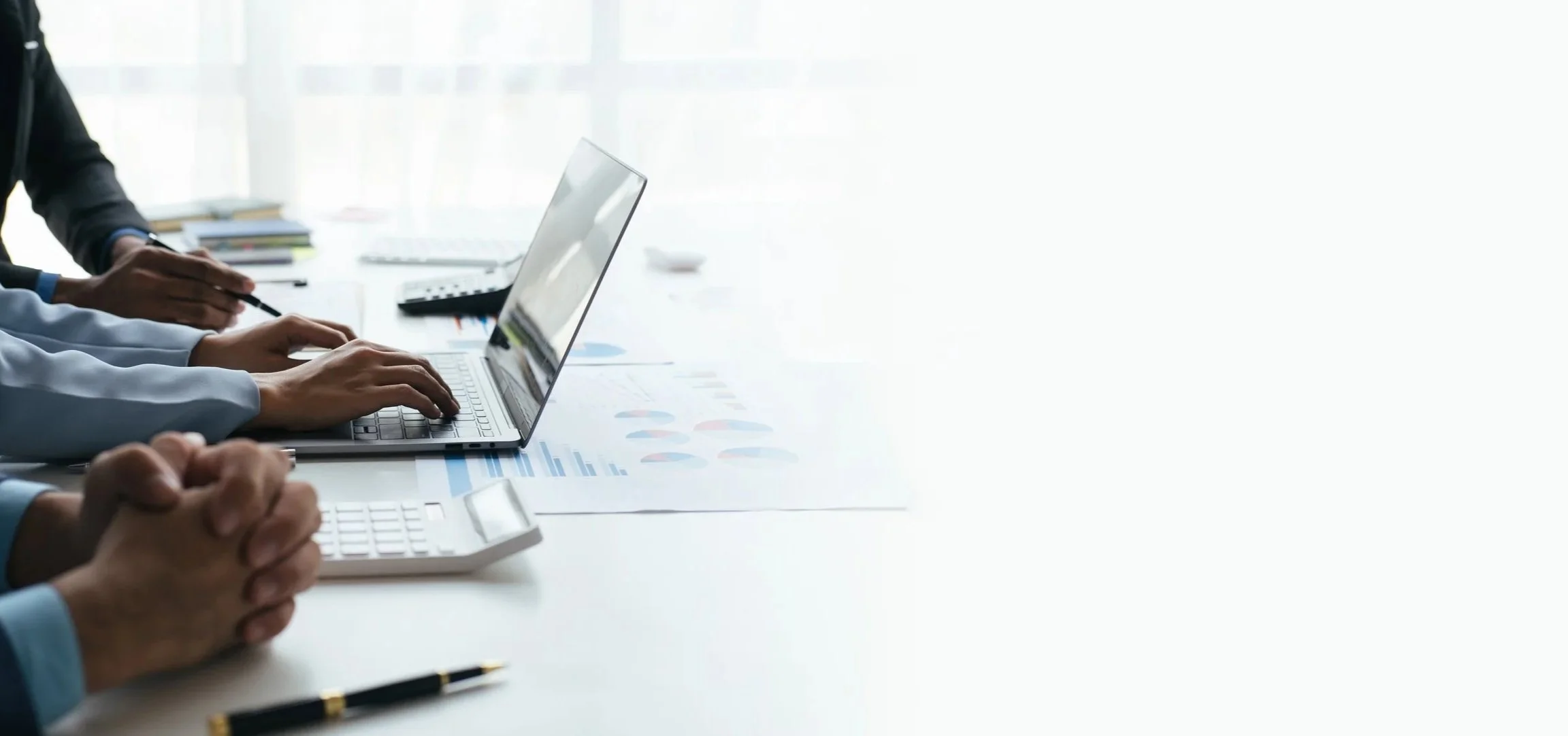 People working on laptops at a conference table with documents and office supplies.