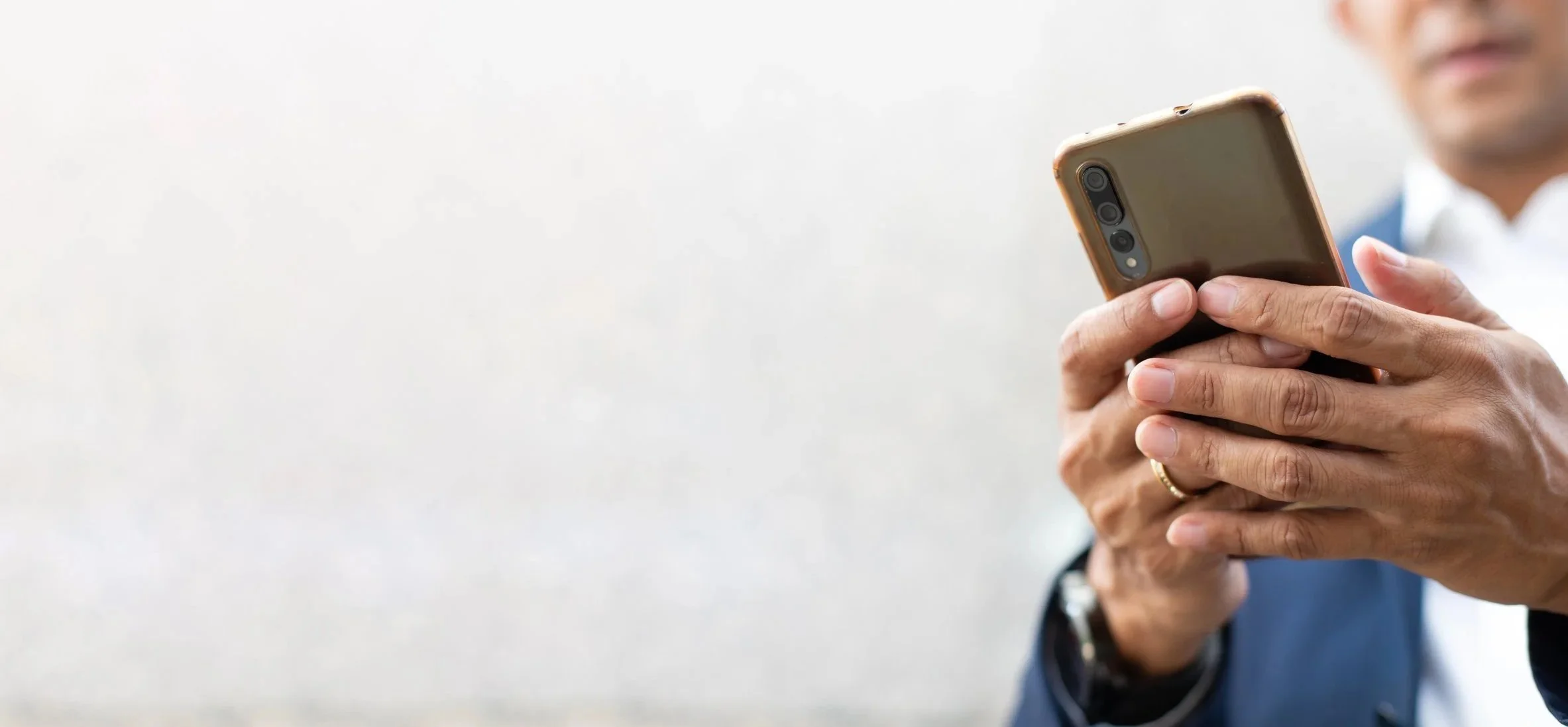 Person wearing a navy suit holding a smartphone in their hands, with a light-colored background.
