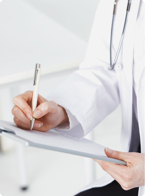 Close-up of a healthcare professional in a white coat writing on a clipboard with a pen in a clinical setting.