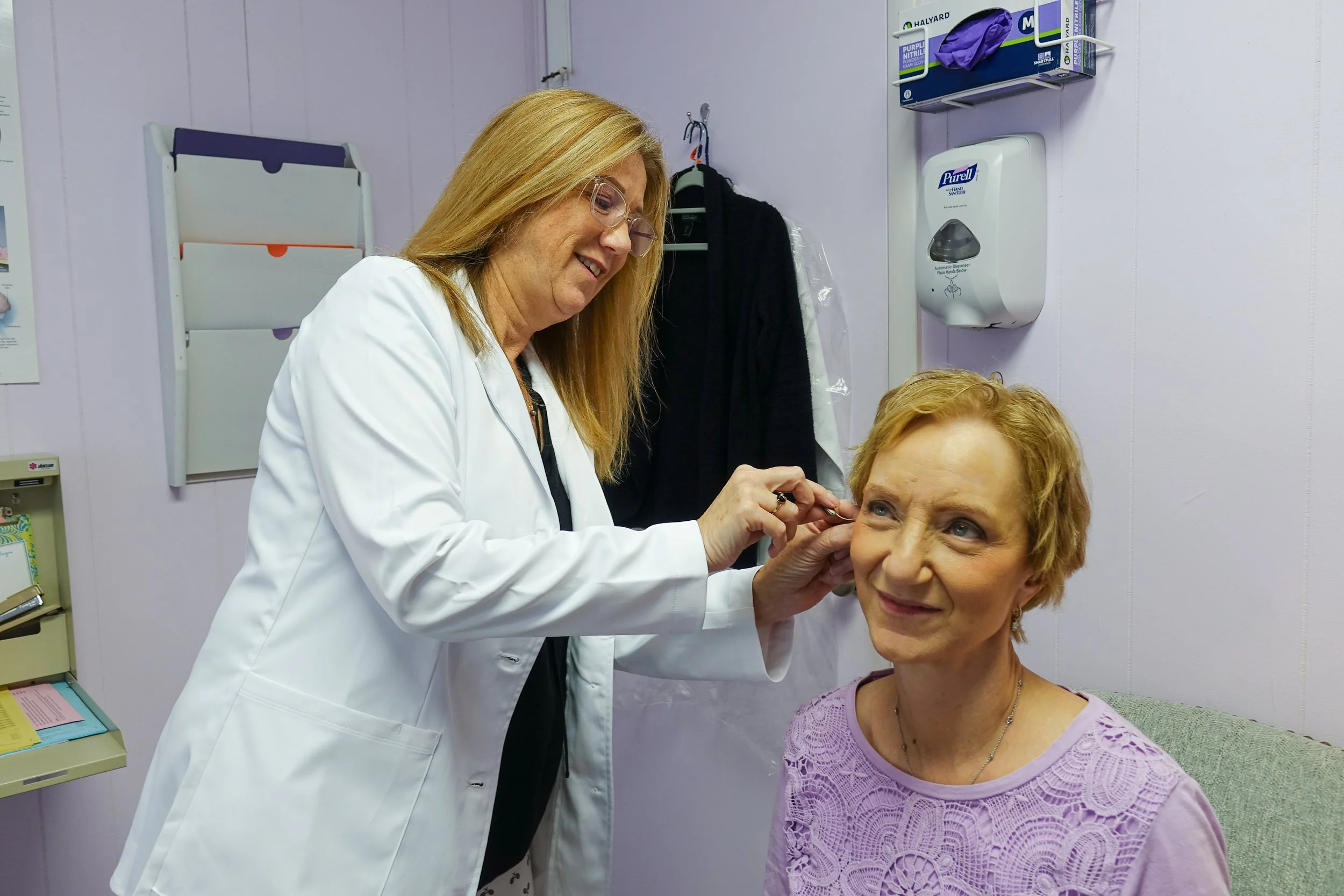 A healthcare professional administering a vaccine or injection to a seated elderly woman in a medical office.