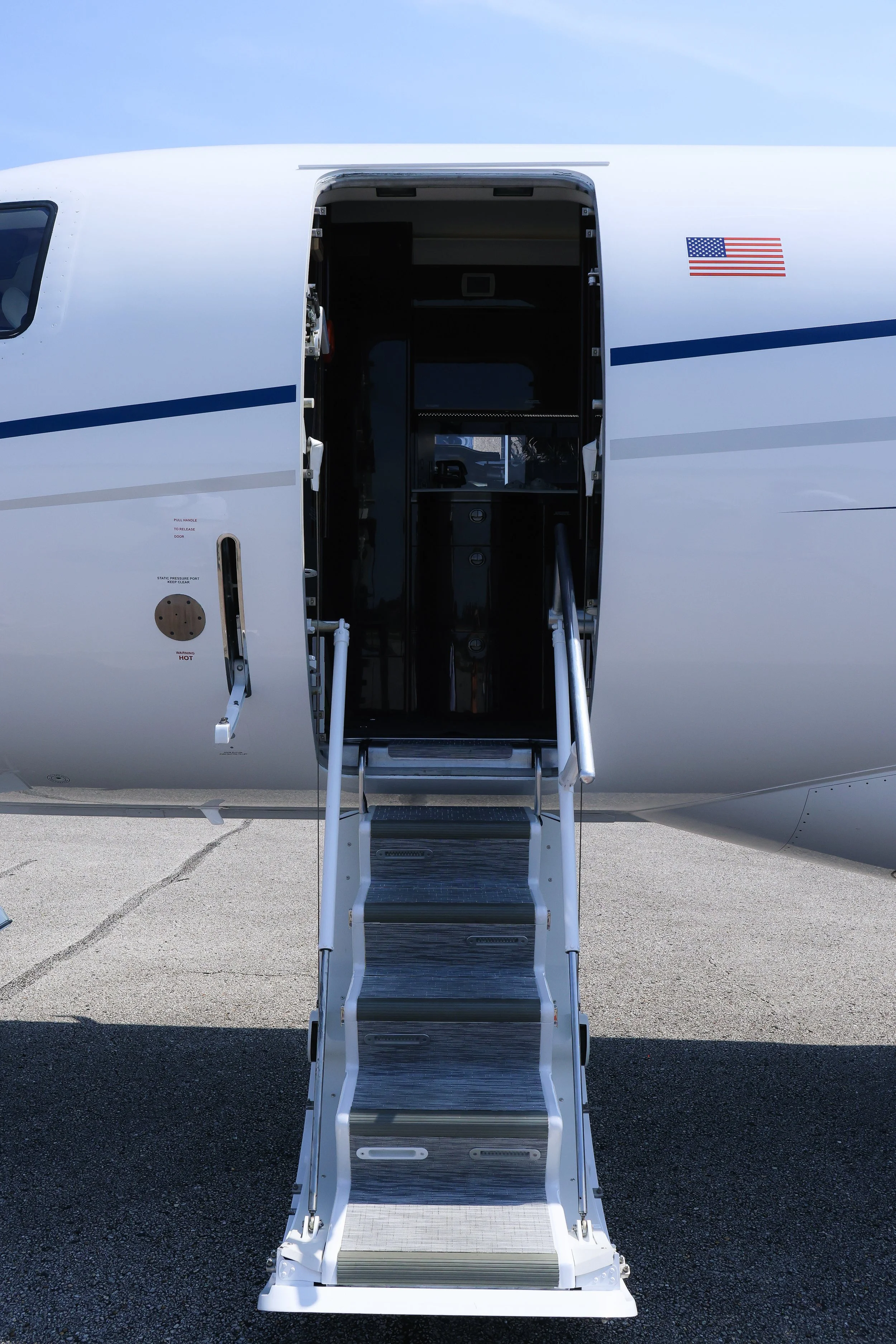 Front view of a private jet with an open door and a retractable staircase leading into the aircraft, American flag decal on the side.