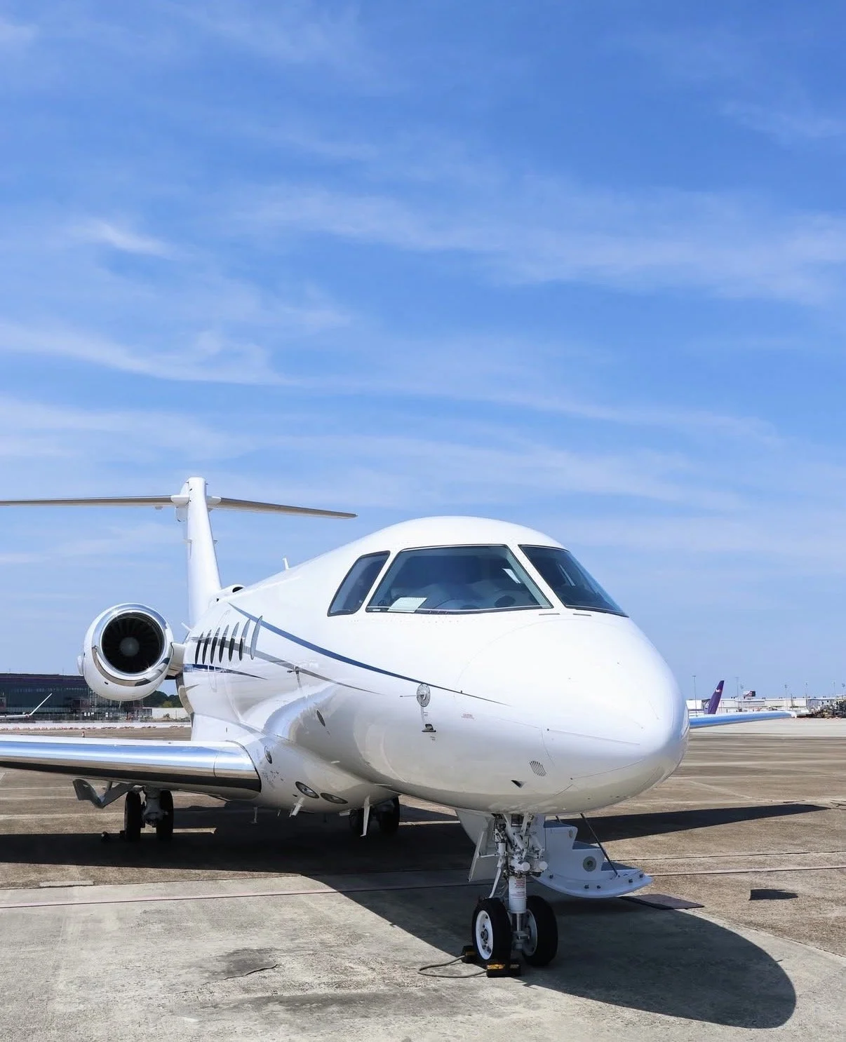 A white private jet parked on the tarmac under a blue sky with some clouds.