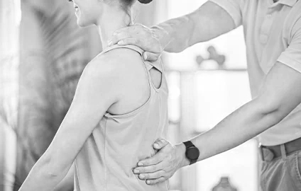 A physical therapist or chiropractor performing a back adjustment on a woman patient in a clinical setting.
