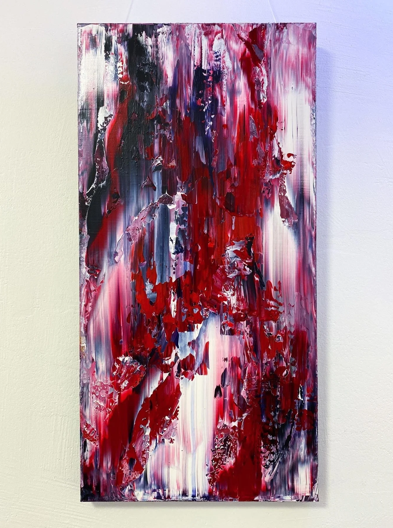 Abstract expressionist painting with bold red, black, white, and purple streaks and patches, mounted on a white wall.