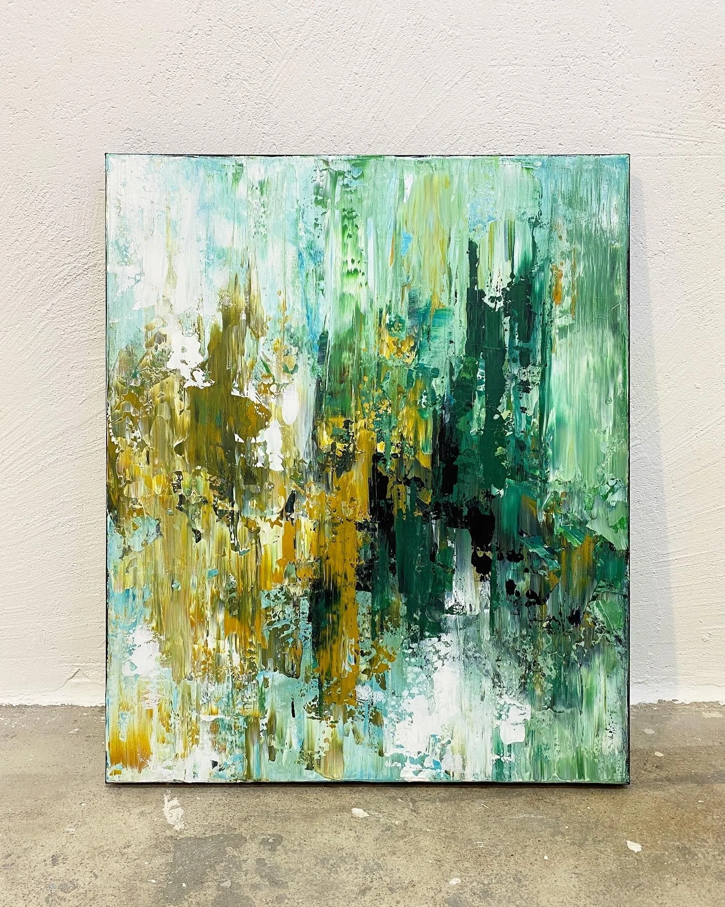 Abstract green, blue, yellow, black, and white painting on a large canvas against a white wall.