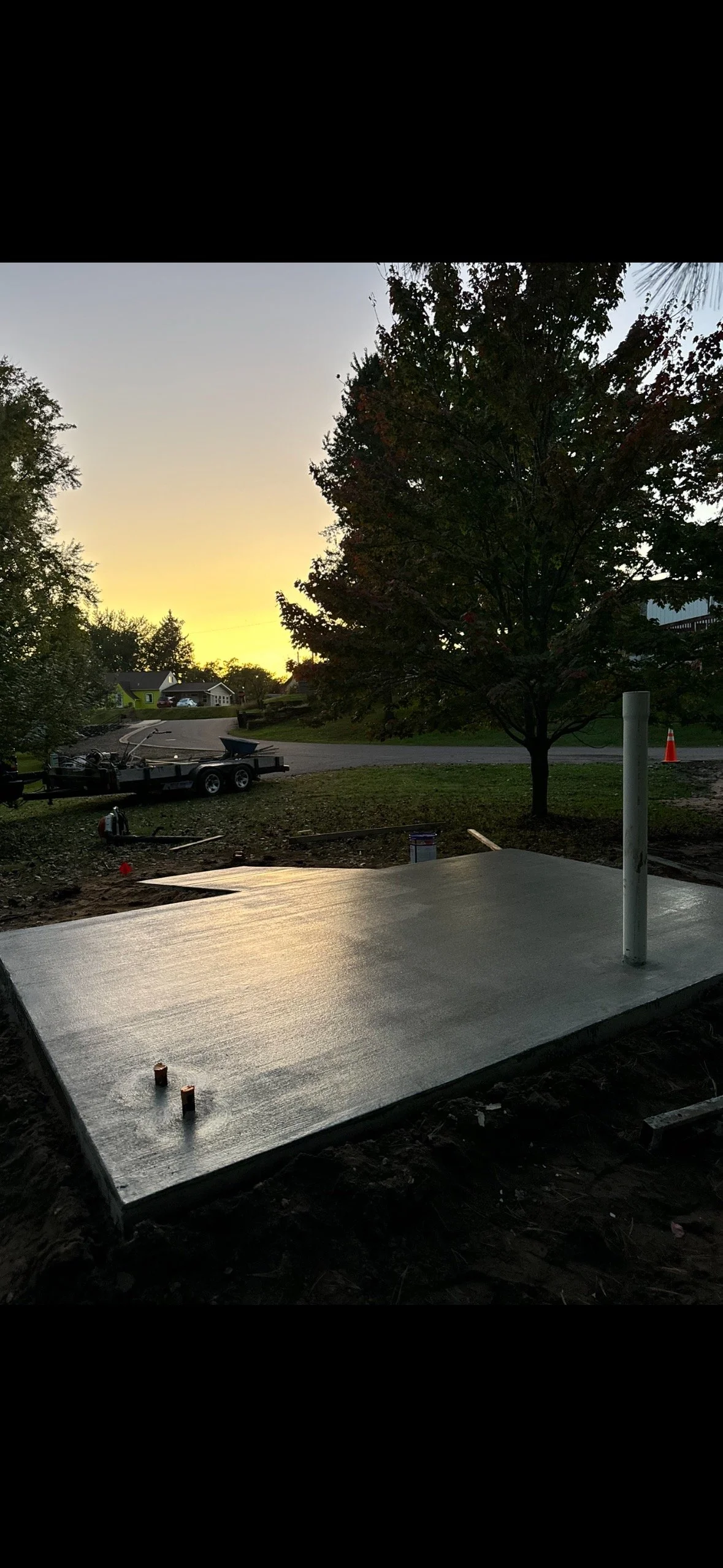 Concrete slab with pipe post and construction tools in yard at sunset.