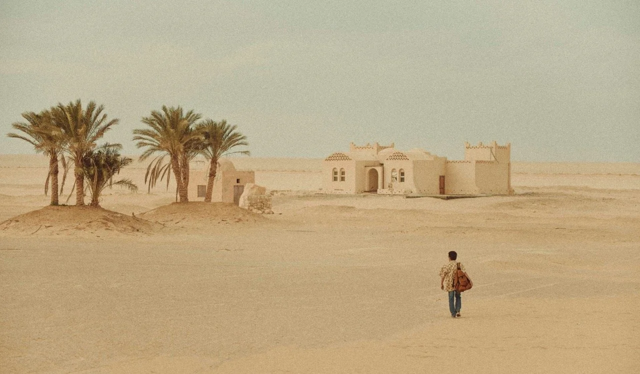 Man walking in the desert towards a building in Morocco.