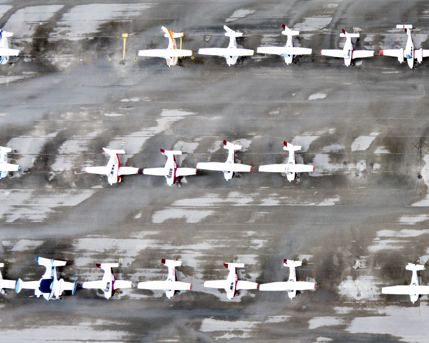 Aerial view of a row of small private airplanes parked on a concrete tarmac.